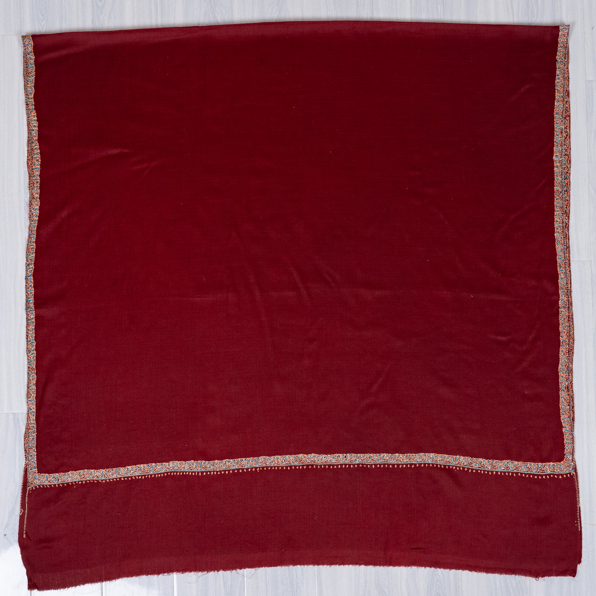 Maroon Merino wool shawl spread flat, with a plain field framed by narrow teal and beige embroidery