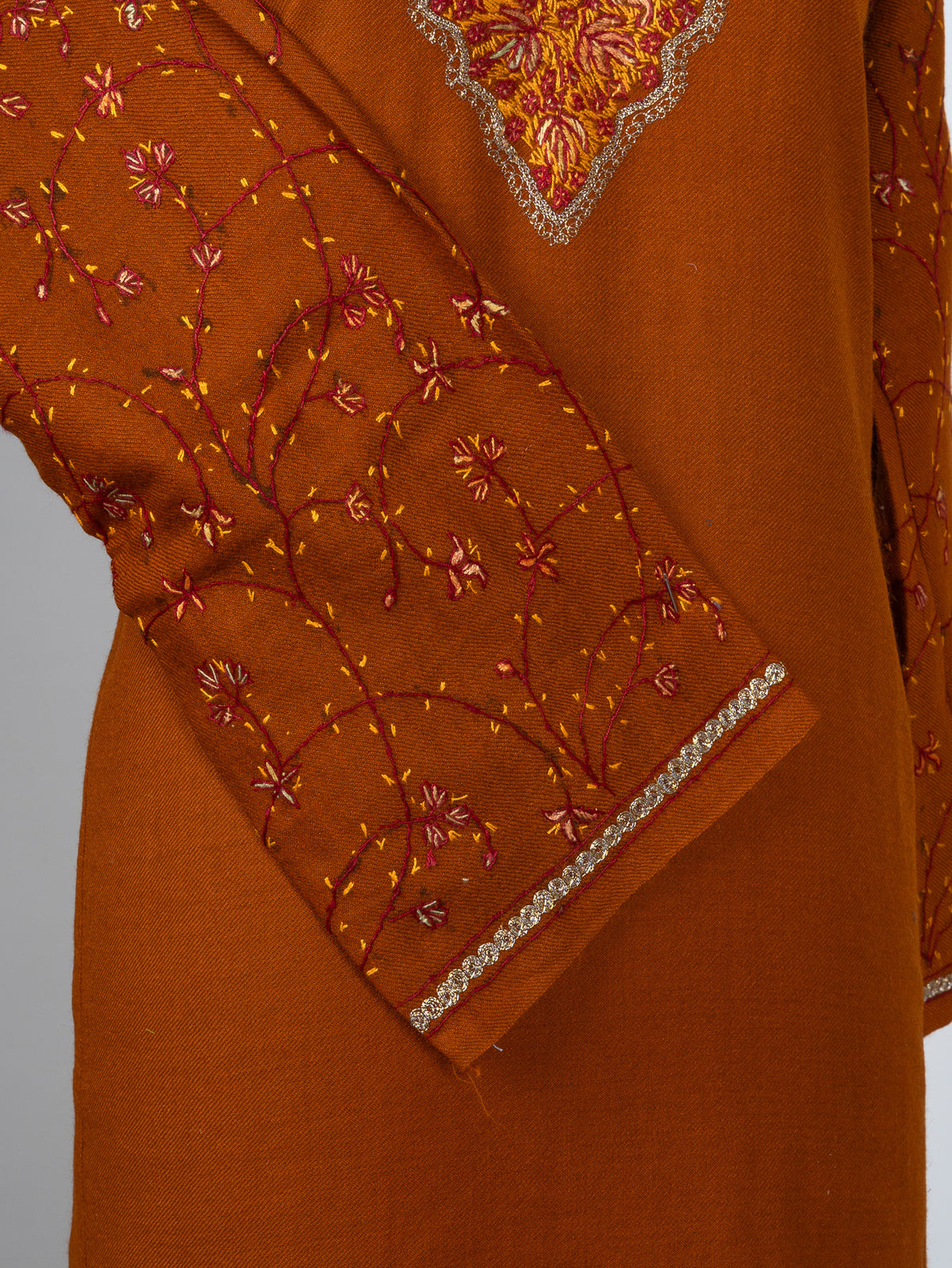 Crossed sleeve of a burnt-orange pheran showing fine red and gold Sozni vines and pale cuff edging