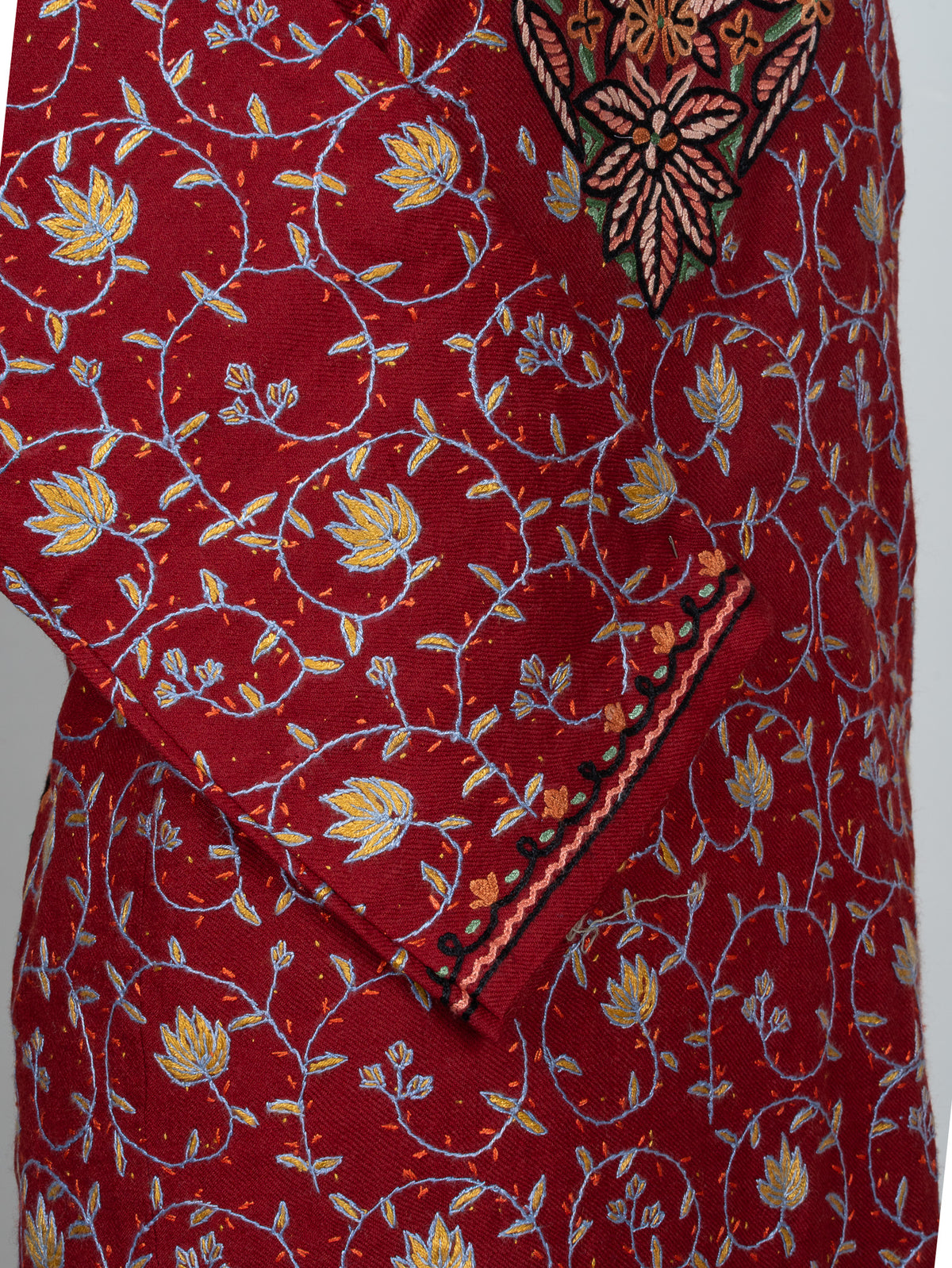 Close-up of the ruby pheran's crossed sleeve with fine yellow and blue floral vines and dark embroidered cuff edging