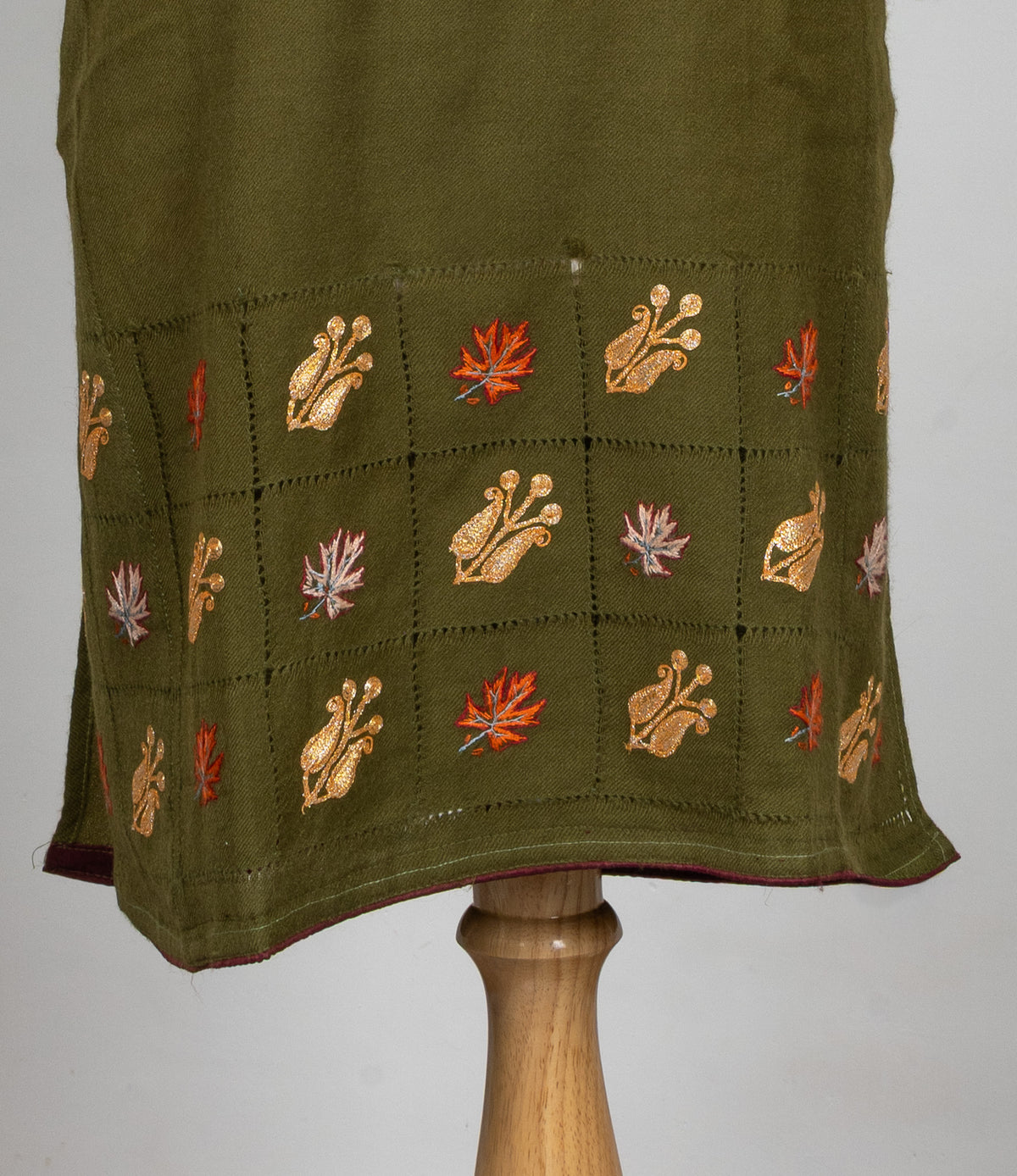 Olive-green pheran hem with golden floral motifs and orange and pale pink leaves arranged in a stitched grid