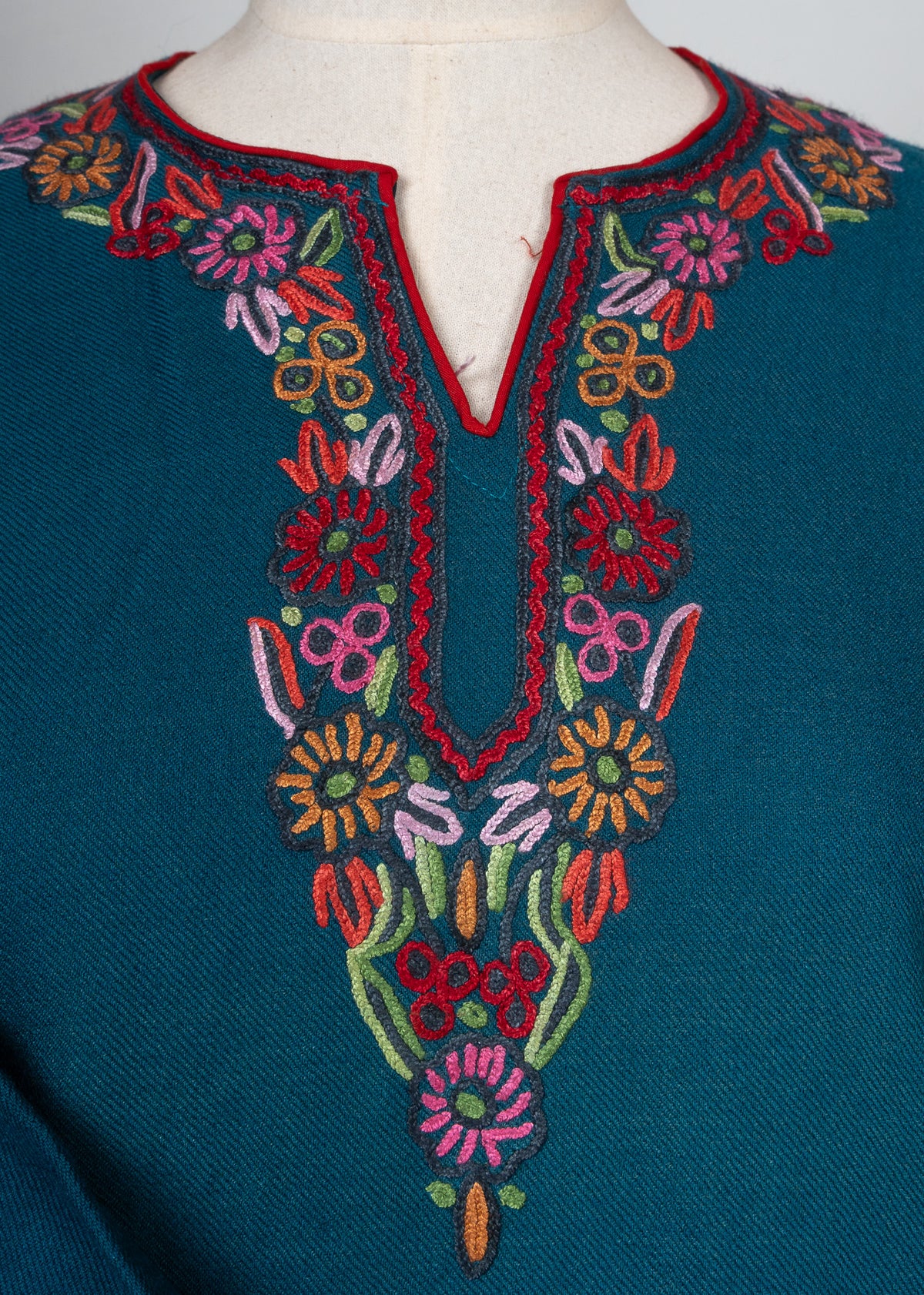 Close-up of pink, orange and green floral embroidery around the teal pheran's split neckline