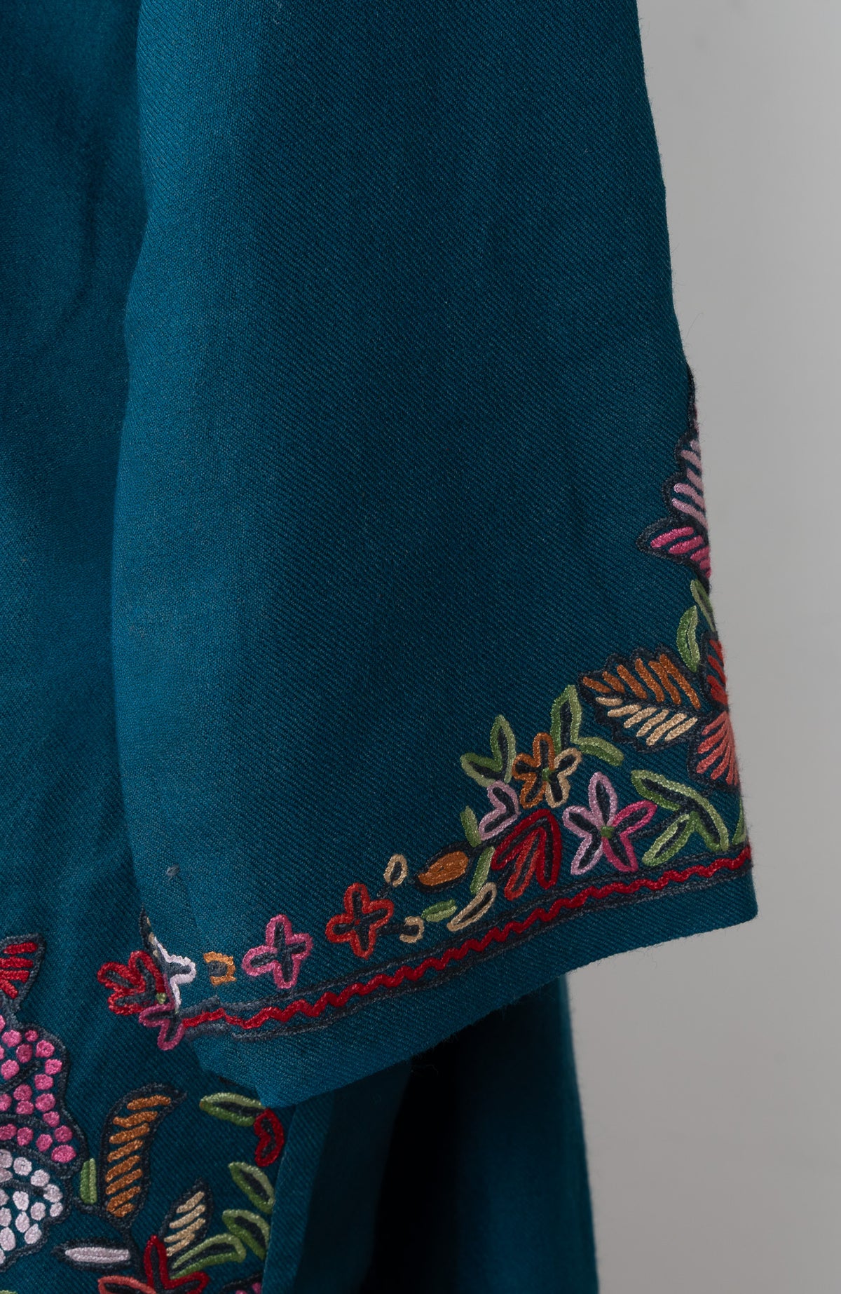 Close-up of the teal pheran's sleeve cuff with colourful embroidered flowers and fine red edging