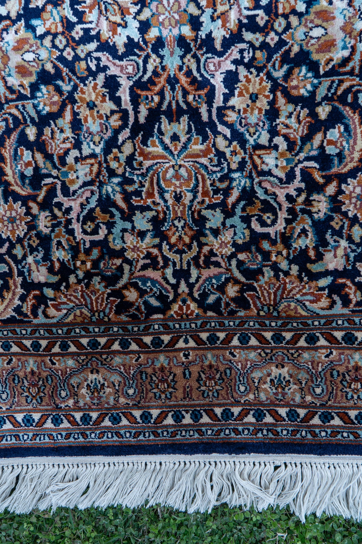 Midnight-blue carpet end with intricate floral motifs, layered borders and white fringe