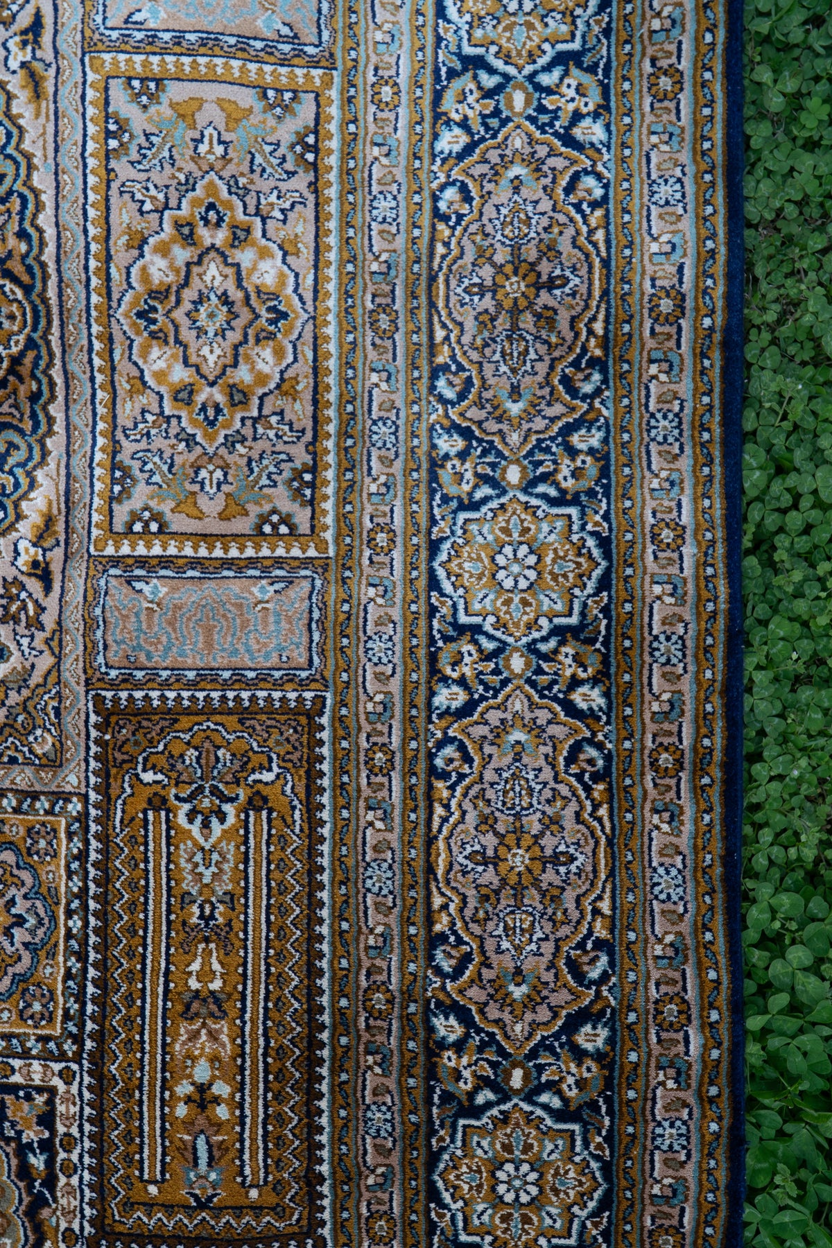 Detail of the carpet's gold and cream ornamental panels beside a wide navy floral border