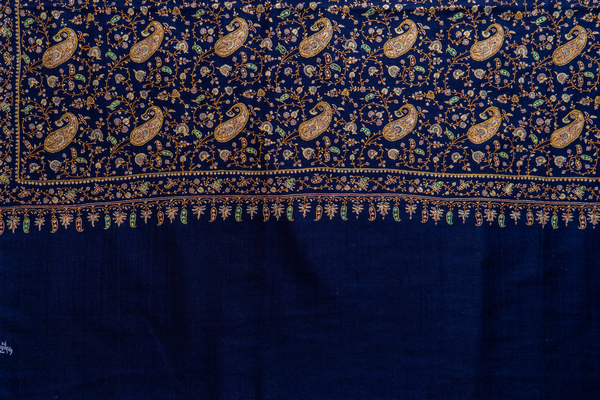 Flat detail of the midnight-blue shawl's fine Sozni border and small hanging motifs above the plain end