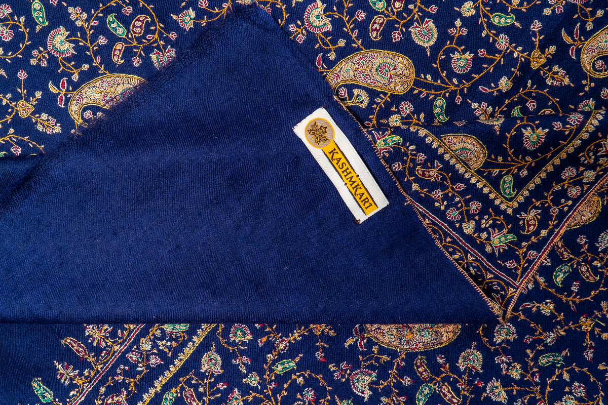 Kashmkari fabric label on a turned-back plain blue corner, surrounded by golden paisleys and fine Sozni floral embroidery