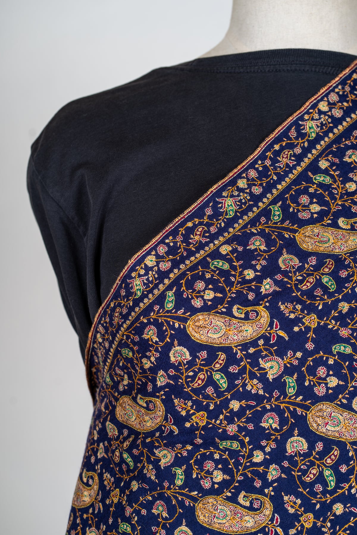 Shoulder detail of the midnight-blue shawl, showing golden paisleys, curling floral stems and a narrow embroidered border