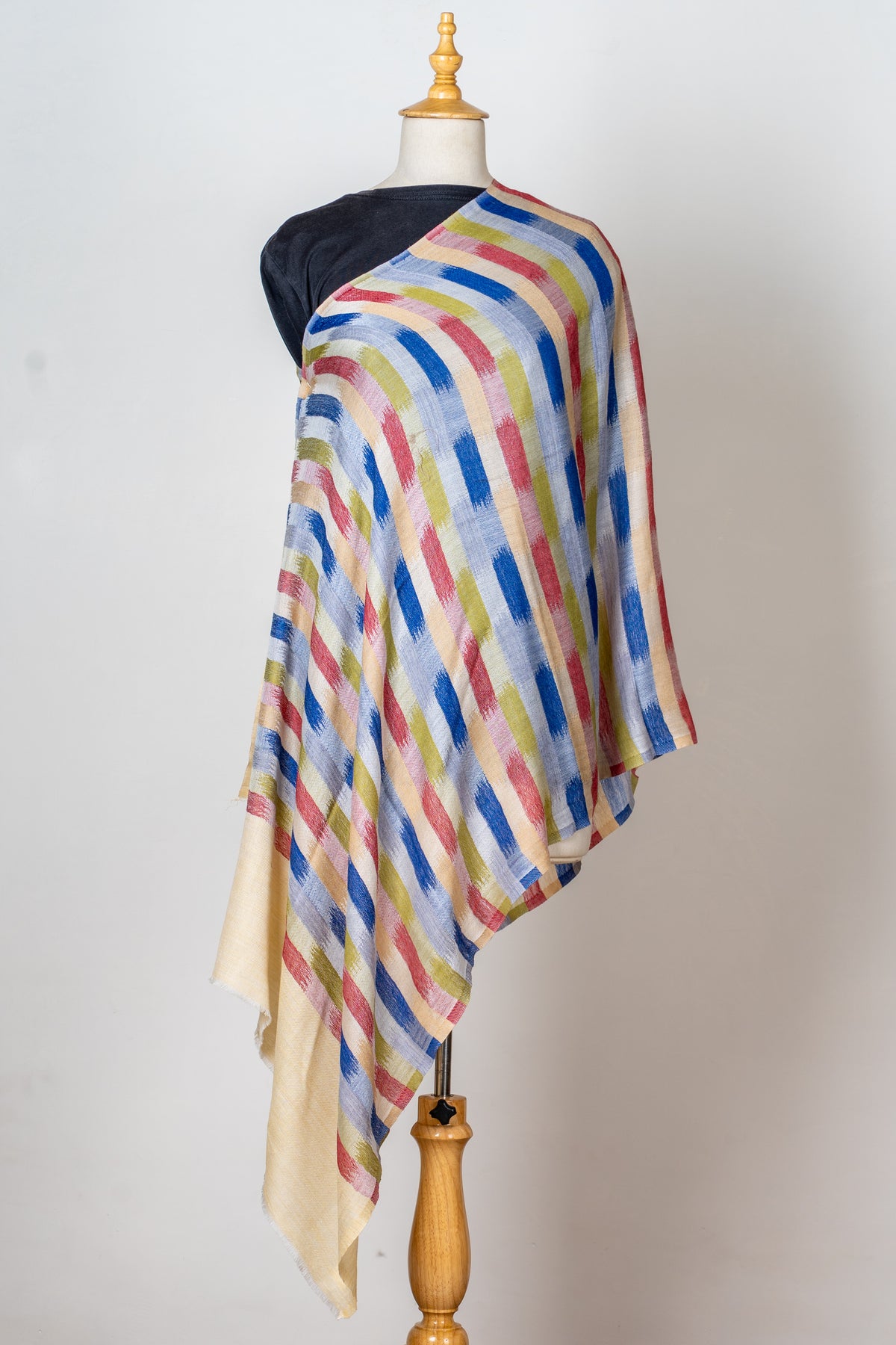 Angled view of the multicoloured striped stole draped diagonally across a mannequin, with plain cream end panels