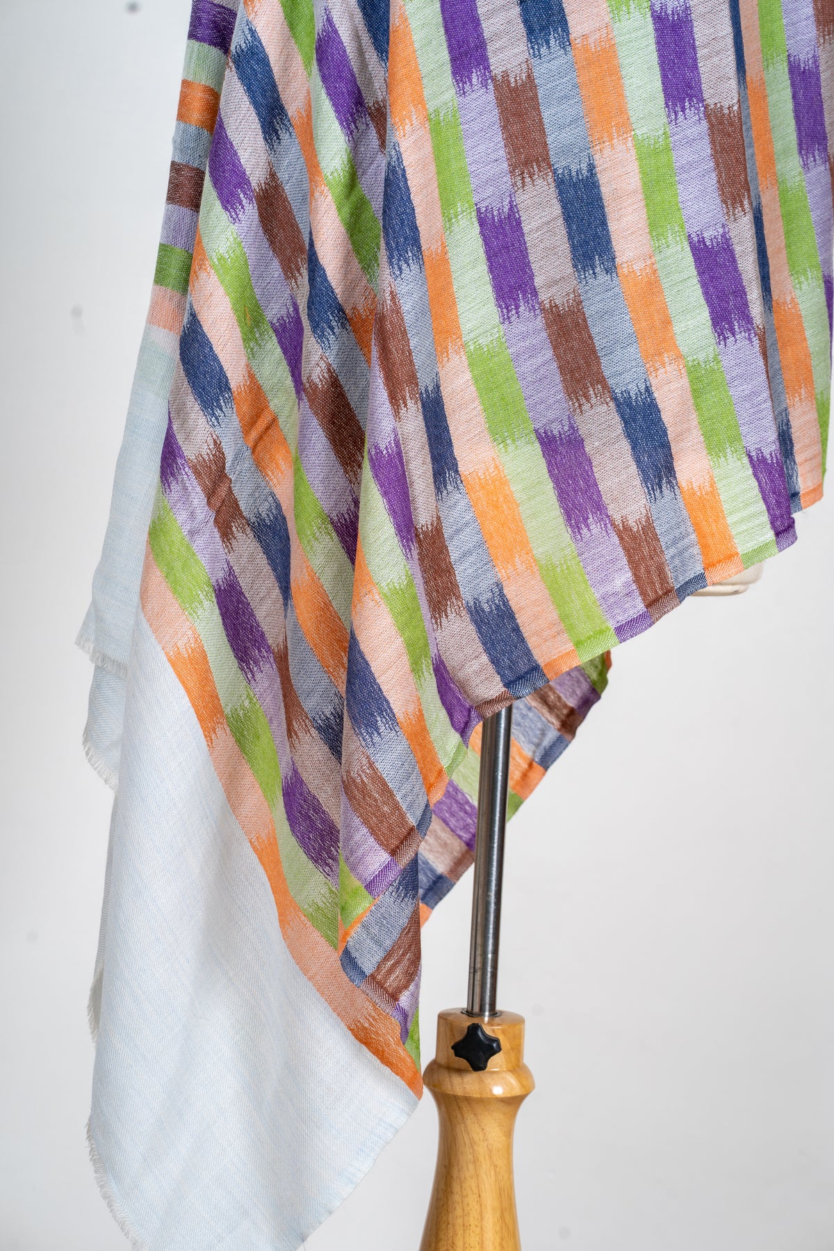 Detail of a multicoloured geometric printed stole falling in folds above a plain pale end panel and short fringe