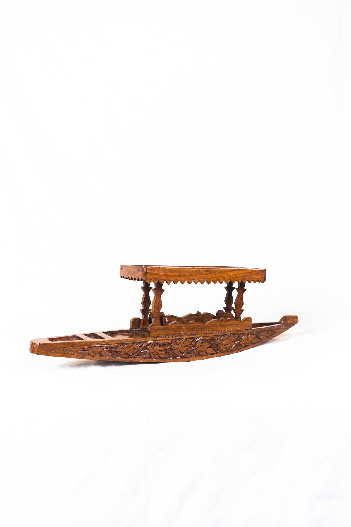 Walnut wood miniature shikara shown from the side, with an open seating area, raised ends and a carved canopy