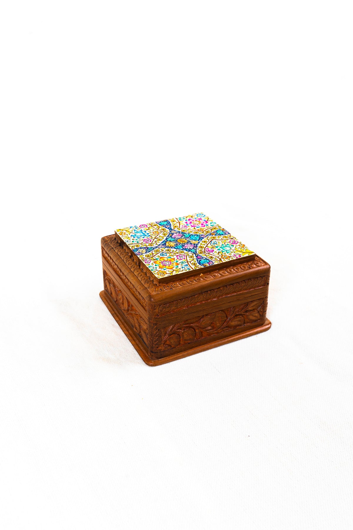 Angled view of the closed walnut wood box, showing its colourful floral lid and carved leafy sides.
