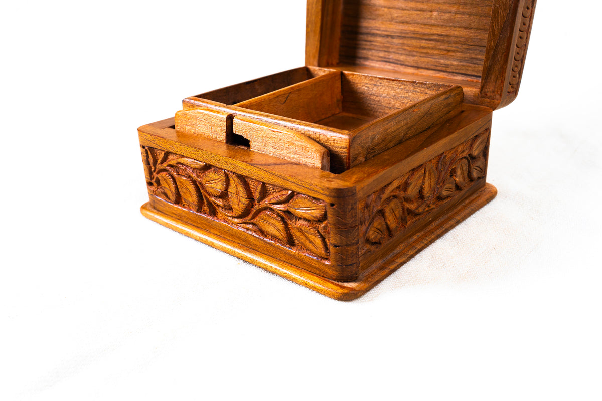 Low angled view of the open walnut wood box, highlighting carved leaves along the sides and the tray inside.
