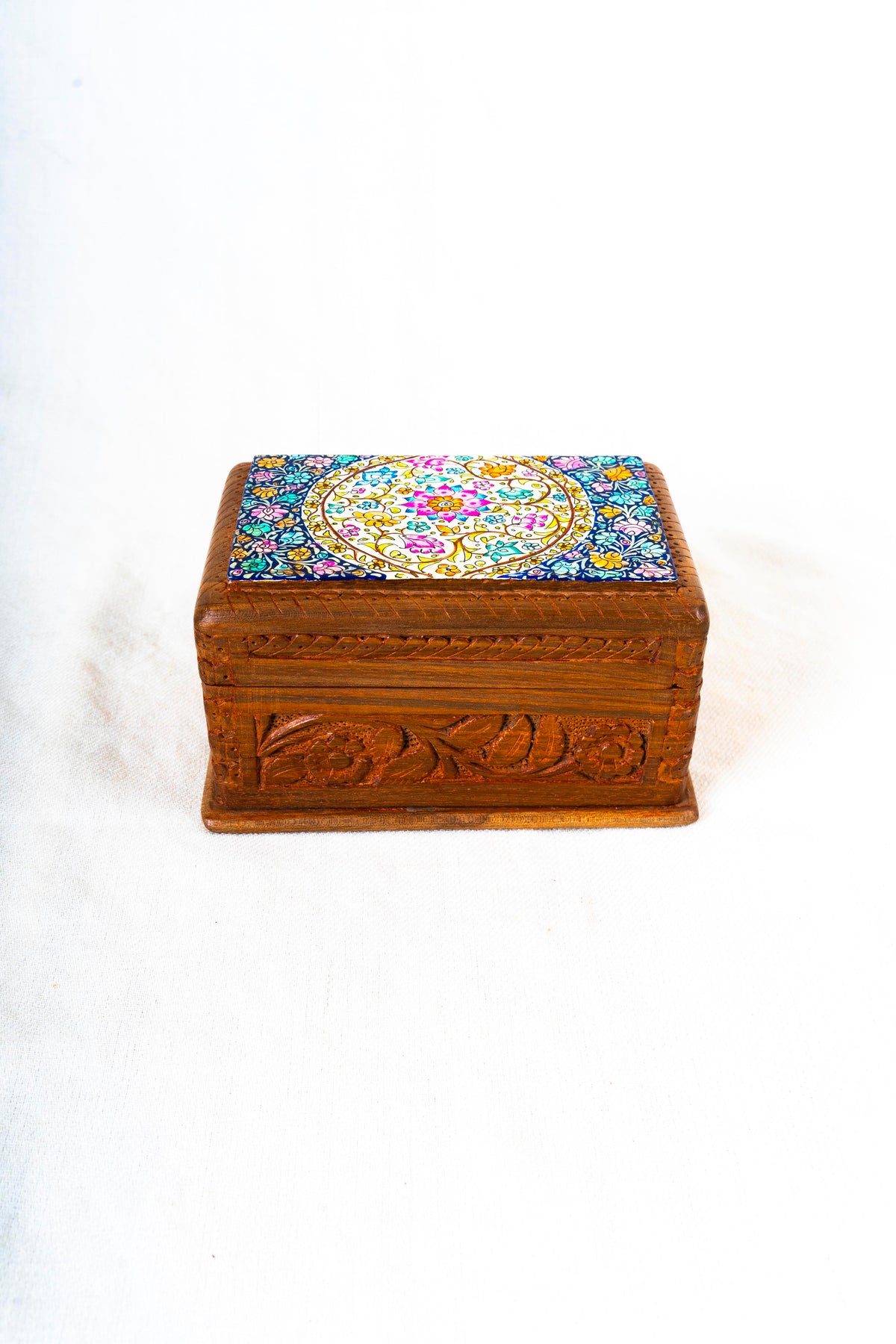 Front view of a closed walnut wood decorative box with carved flowers and leaves below its colourful floral lid