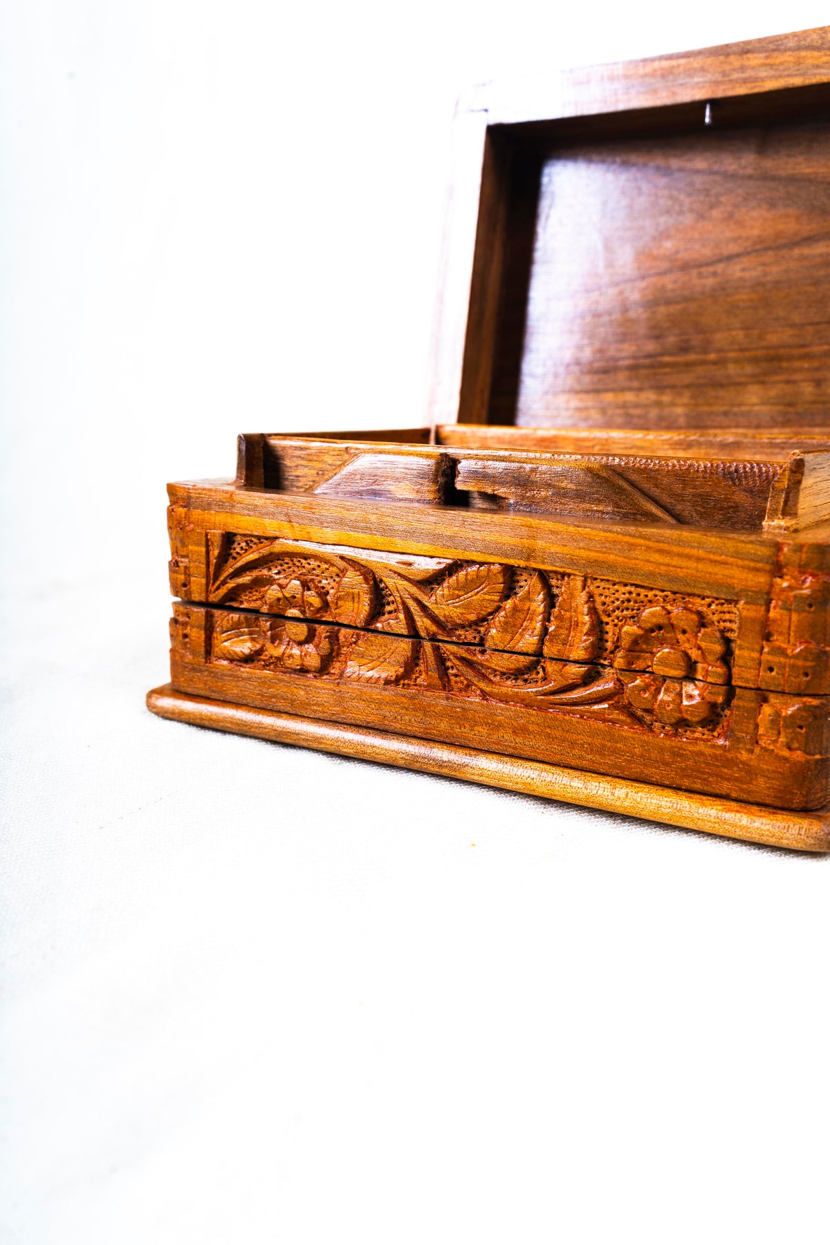 Low close-up of the carved floral front of an open walnut wood box, with its raised lid visible behind