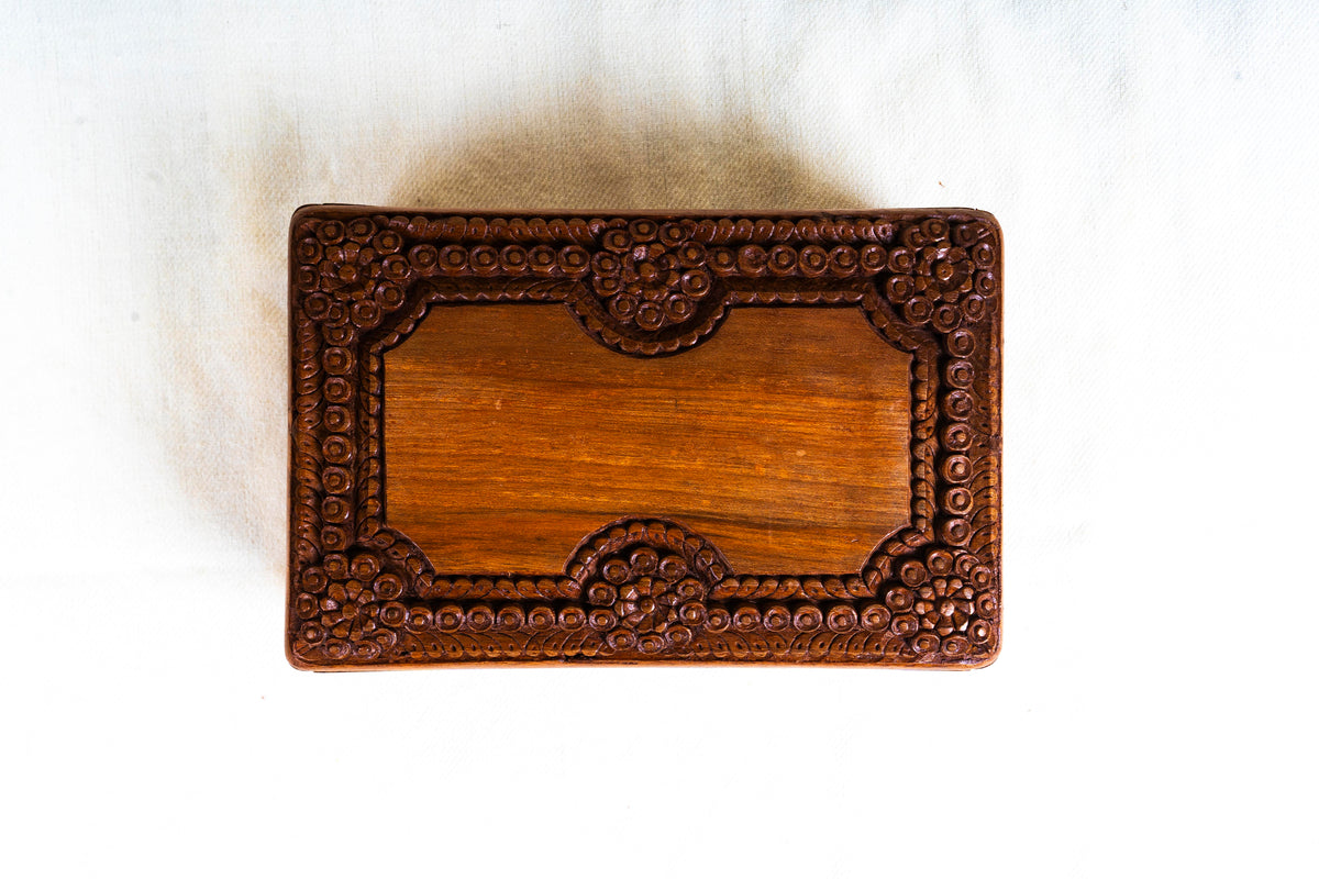 Top view of the walnut box lid, with a plain rectangular centre and a carved border of rosettes and circular motifs.