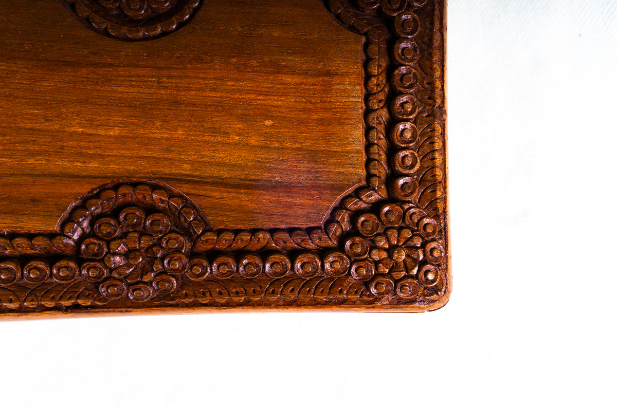 Close-up of the box lid corner showing carved rosettes and rows of small circles around the polished wood centre.