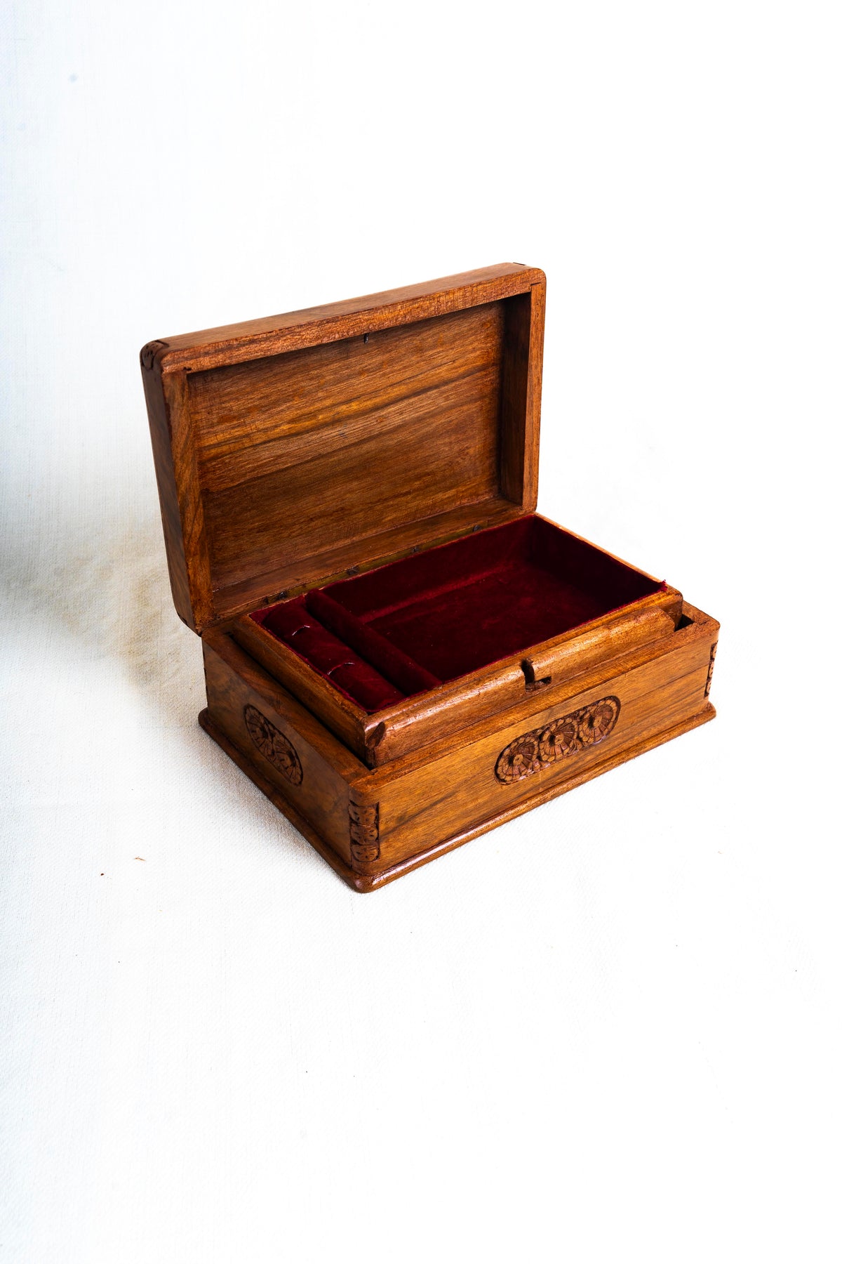 Angled view of the open walnut box with red velvet lining, a narrow side compartment and floral carving on the front.
