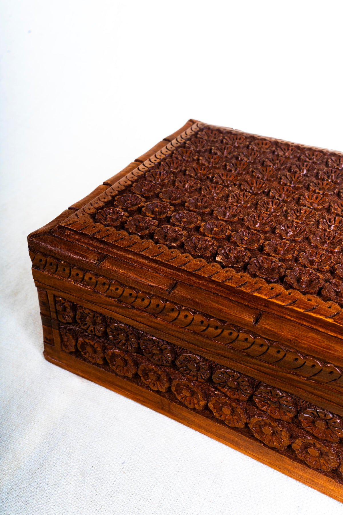Angled corner detail of the walnut jewellery box with carved flowers on the lid and side panels
