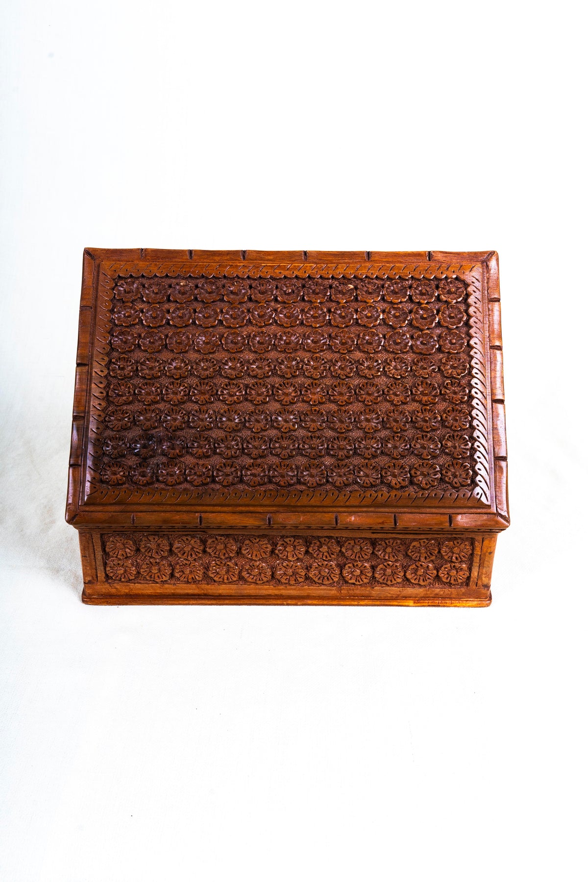Closed walnut jewellery box seen from above at an angle with dense floral carving across the lid and sides