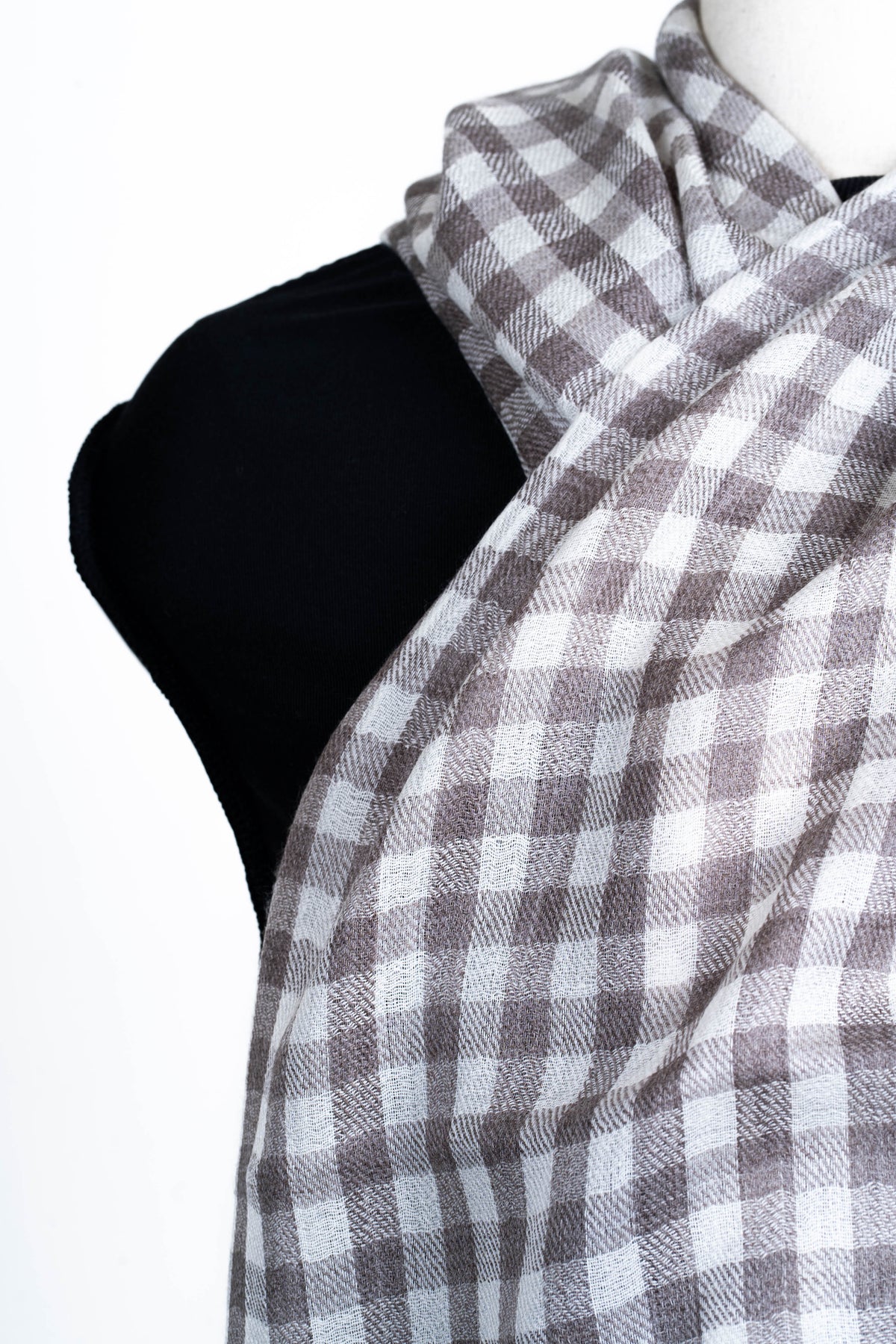 Close-up of the taupe and white checked stole crossed at the neck, showing the fine woven texture.