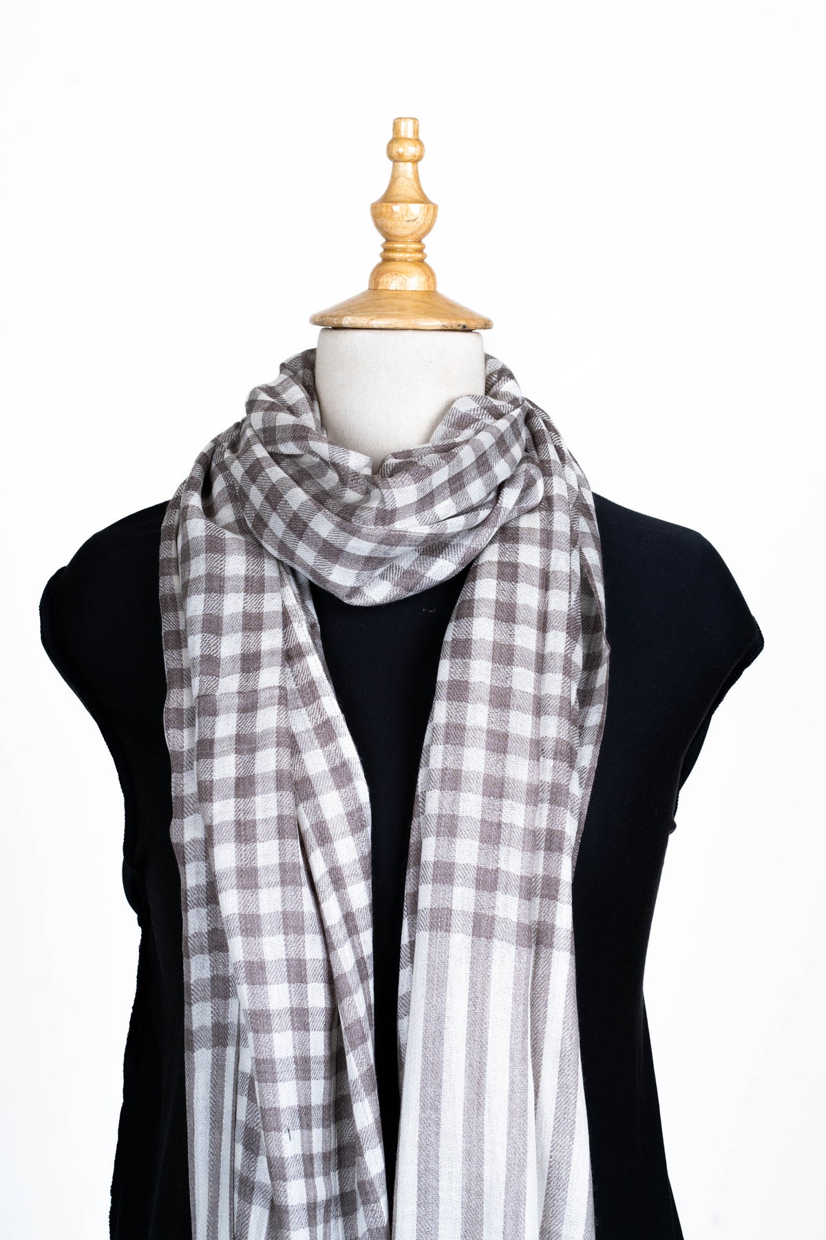 Upper view of the checked merino wool stole loosely looped at the neck, with long striped ends over a black top.