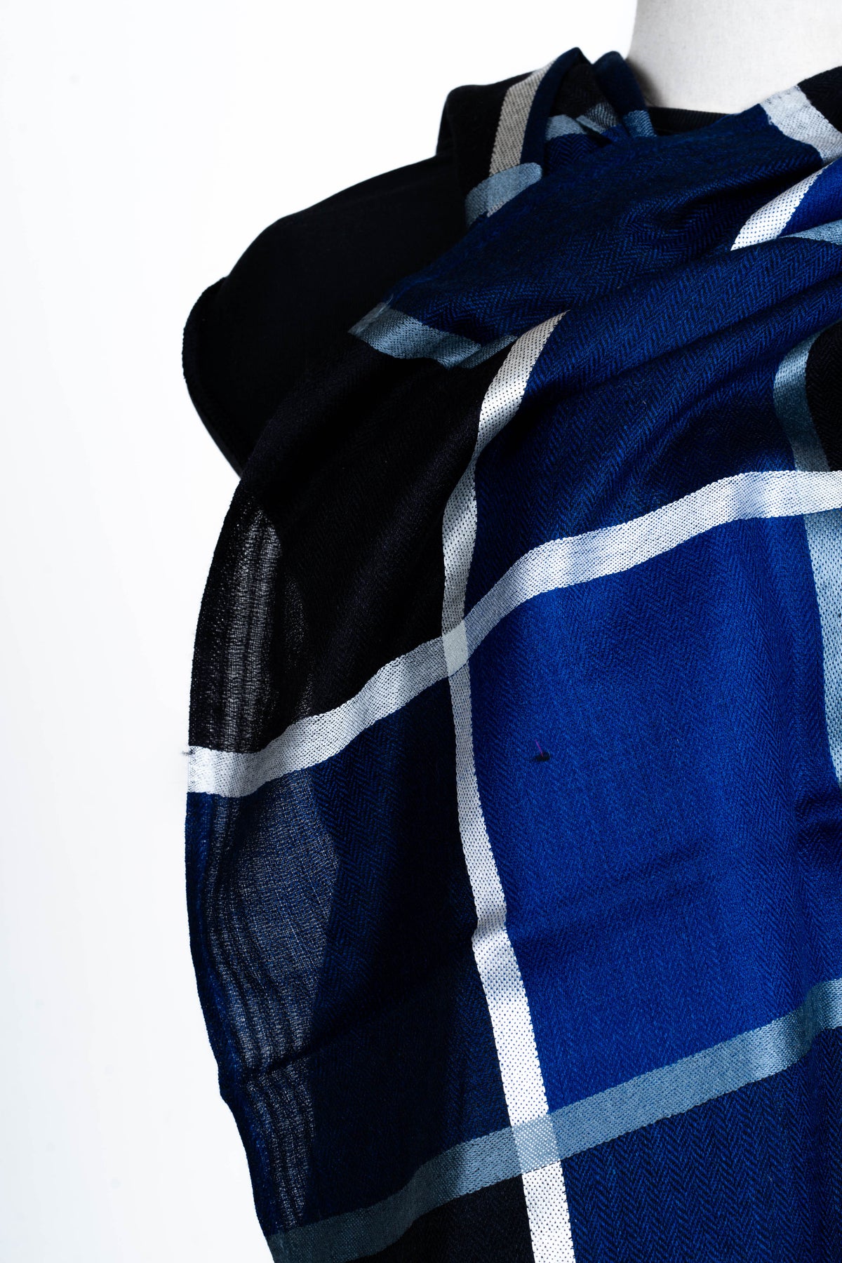 Close-up of blue and black Merino wool folds across a mannequin’s chest, crossed by white and pale blue lines
