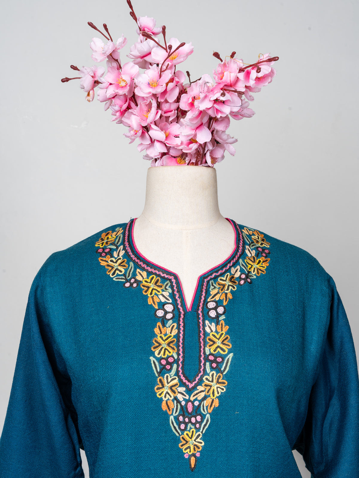 Upper front of a teal Merino wool pheran with yellow, pink, orange and pale green flowers around a notched neckline