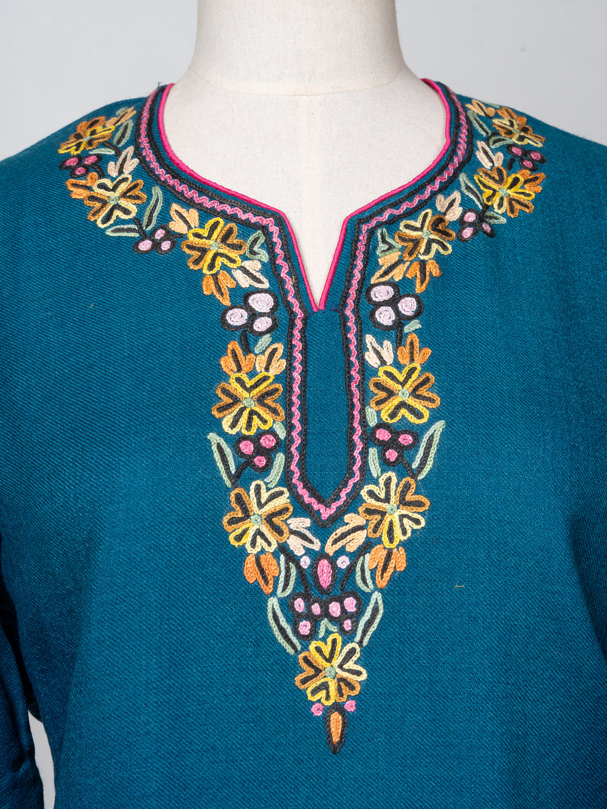Close-up of a teal pheran neckline with yellow and orange Sozni flowers, pale green leaves and pink edging