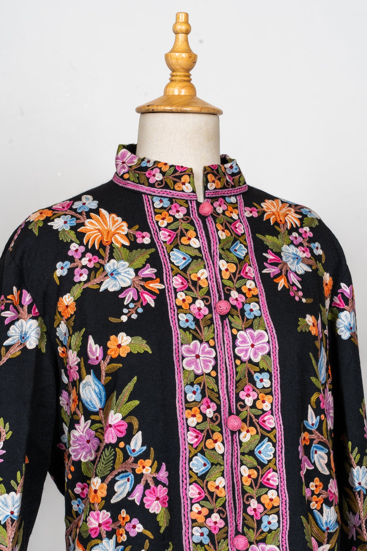 Angled close view of the black jacket’s embroidered stand collar and colourful floral front with pink covered buttons