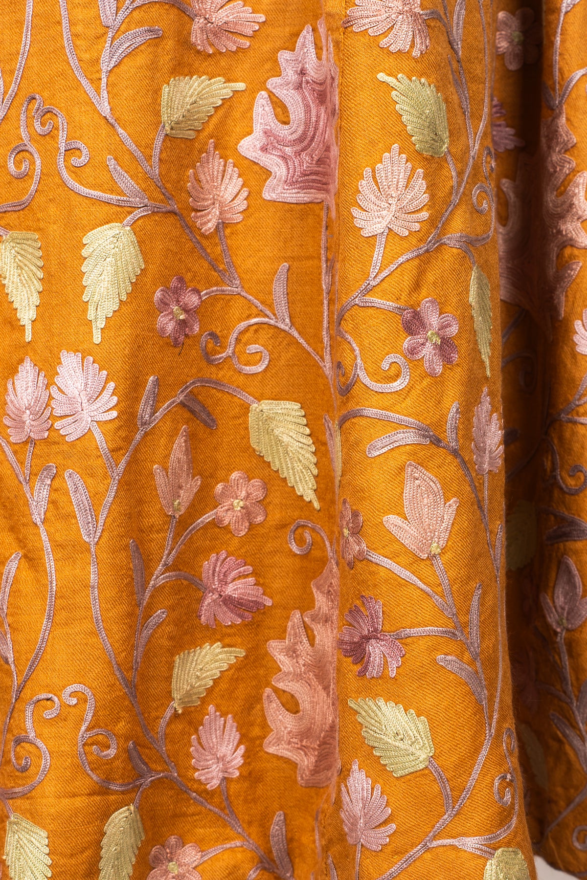 Close-up of lilac and pale green Aari leaves and small flowers on the folds of amber fabric