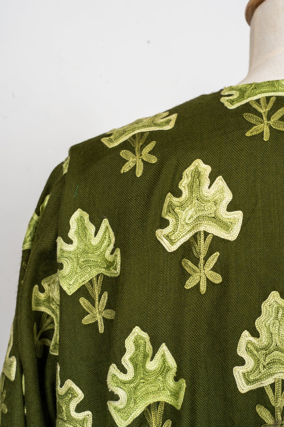 Shoulder close-up of the olive abaya showing repeated pale green embroidered leaves with small branching stems.