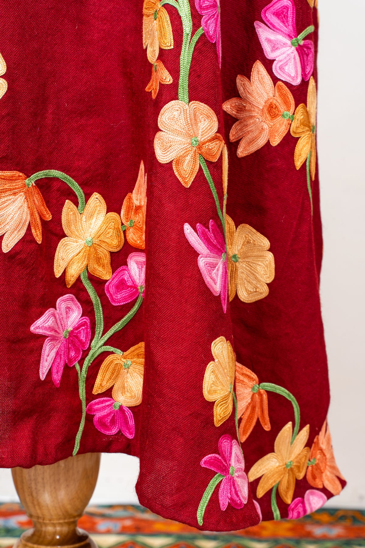 Close-up of pink and orange embroidered flowers and green stems around the crimson abaya’s hem