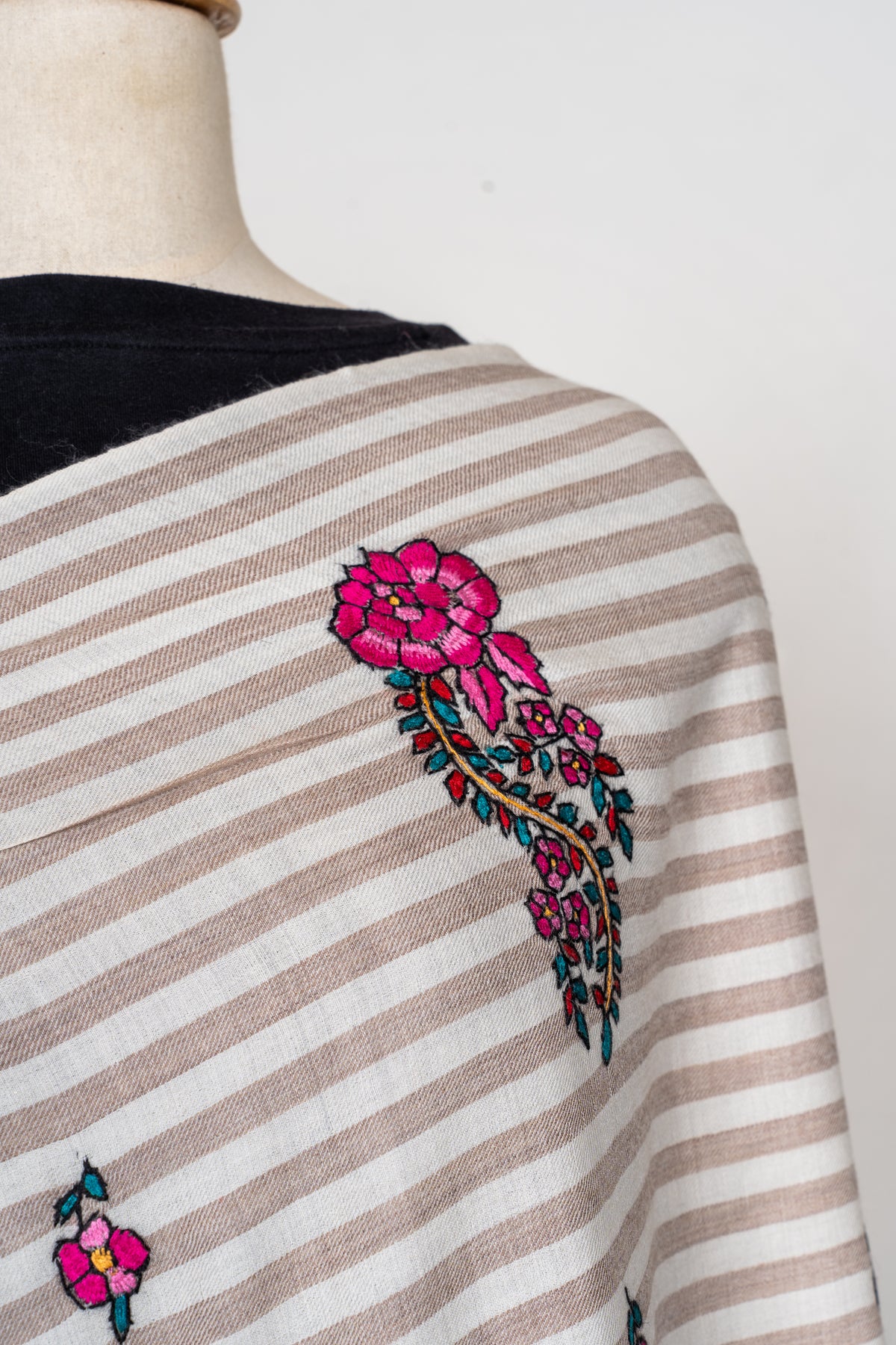 Close-up of a fuchsia flower and curling teal-leaved paisley motif on the shawl’s beige and ivory stripes