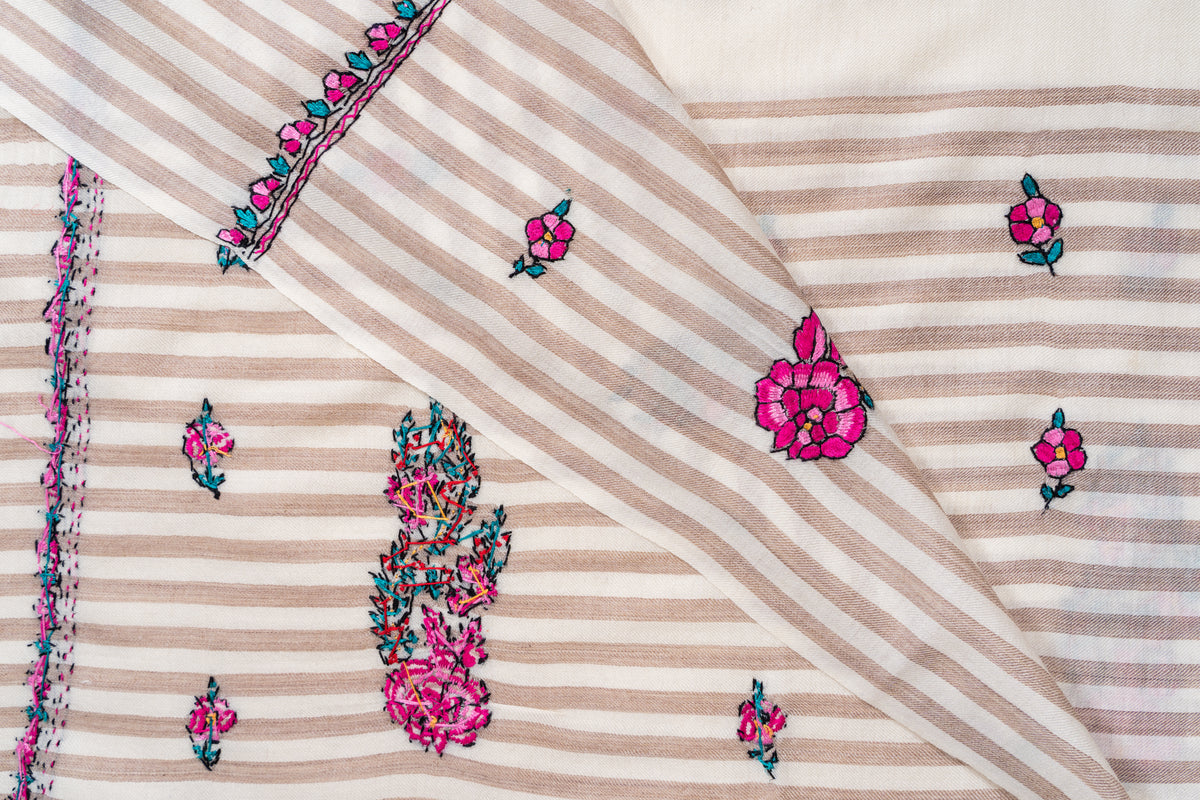 Overlapping folds of the striped ivory shawl showing fuchsia flowers, teal leaves and exposed reverse embroidery