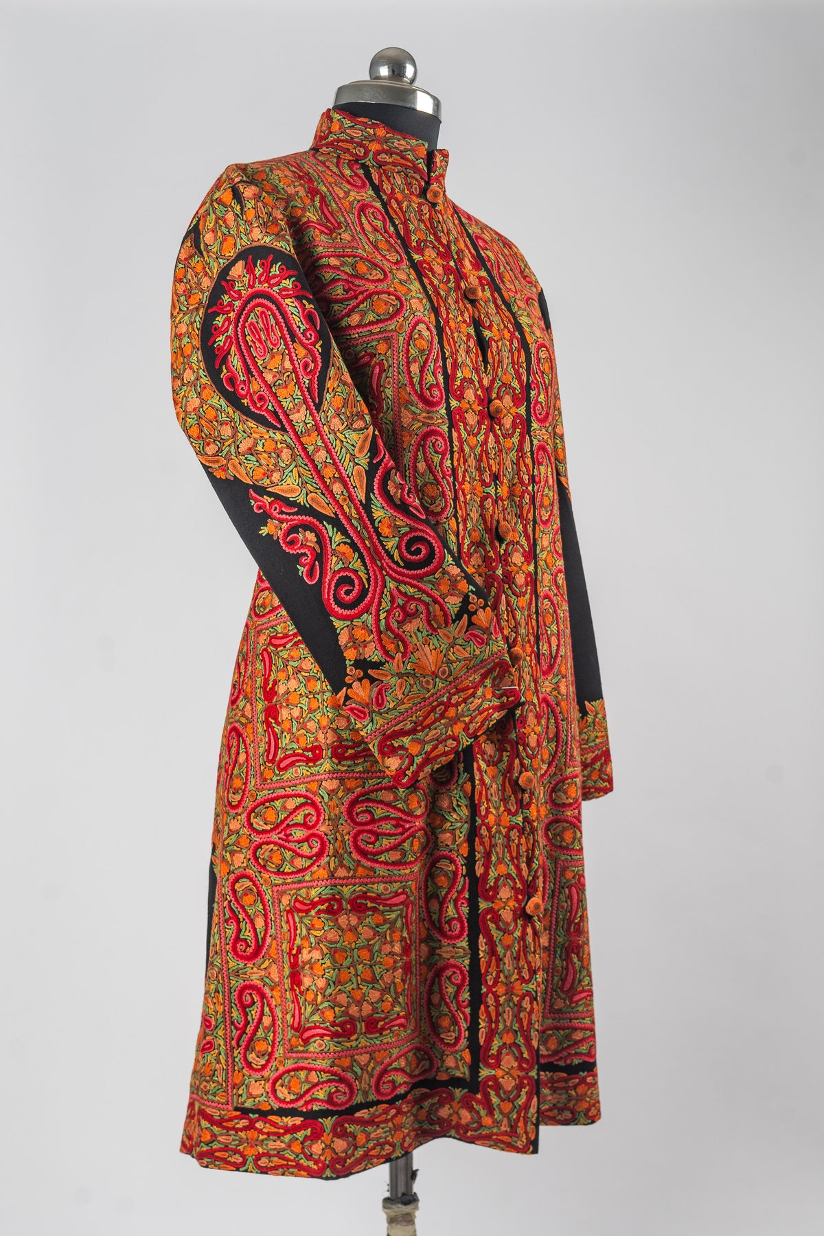 Full angled view of a black Merino wool jacket with red and orange Aari paisley panels and an ornate motif along the sleeve