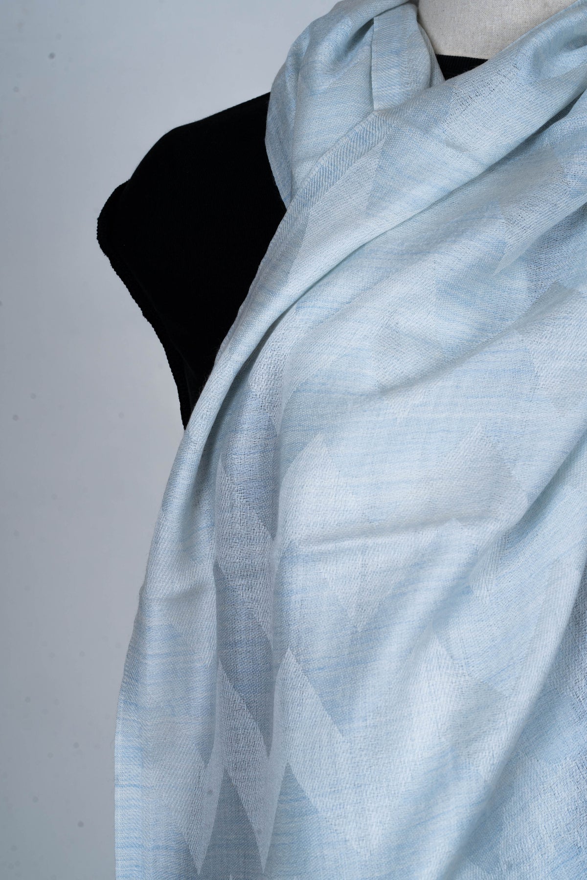 Close-up of the pale blue stole crossed at the neck, with soft folds and a faint geometric woven pattern.
