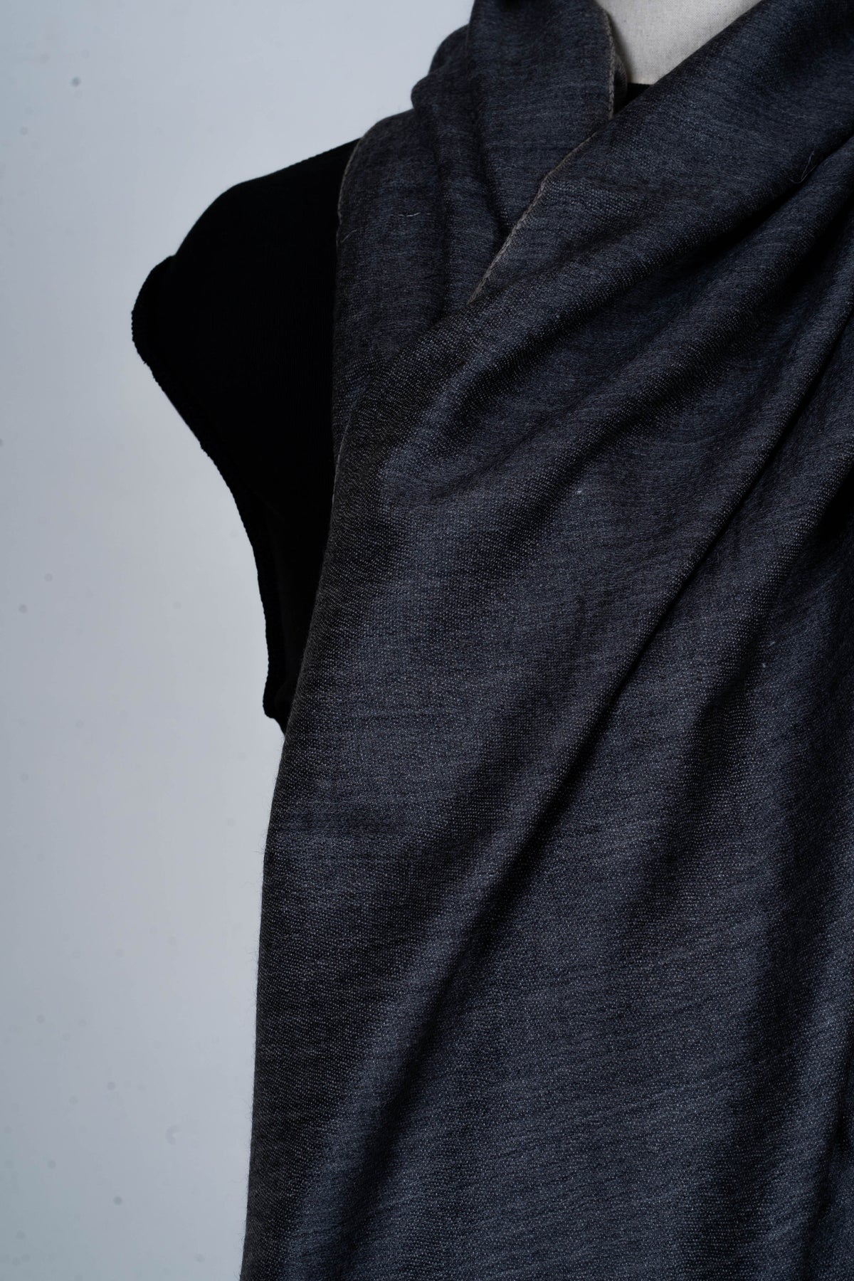 Close-up of a charcoal-grey Merino wool stole folded across a mannequin's chest, showing its fine woven texture