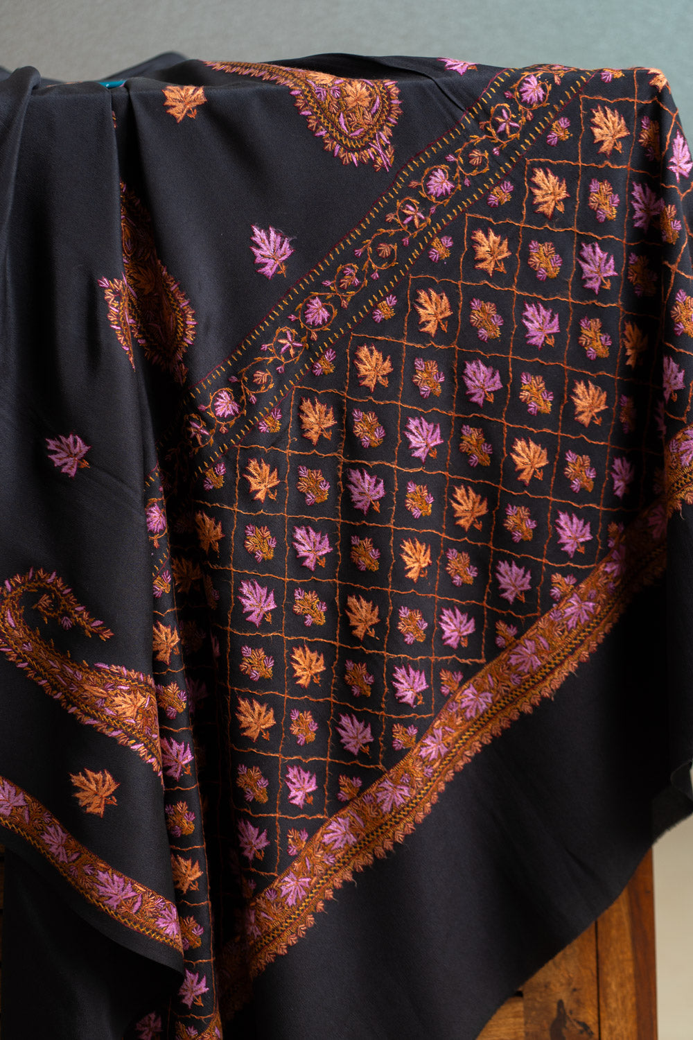 Black crepe saree pallu draped over a wooden screen, showing pink and orange Sozni motifs inside a diagonal grid