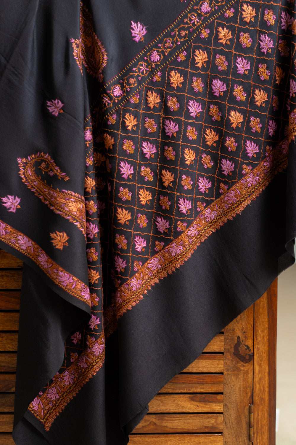 Black crepe saree draped diagonally, displaying a pink and orange Sozni grid panel beside paisleys and leaf motifs