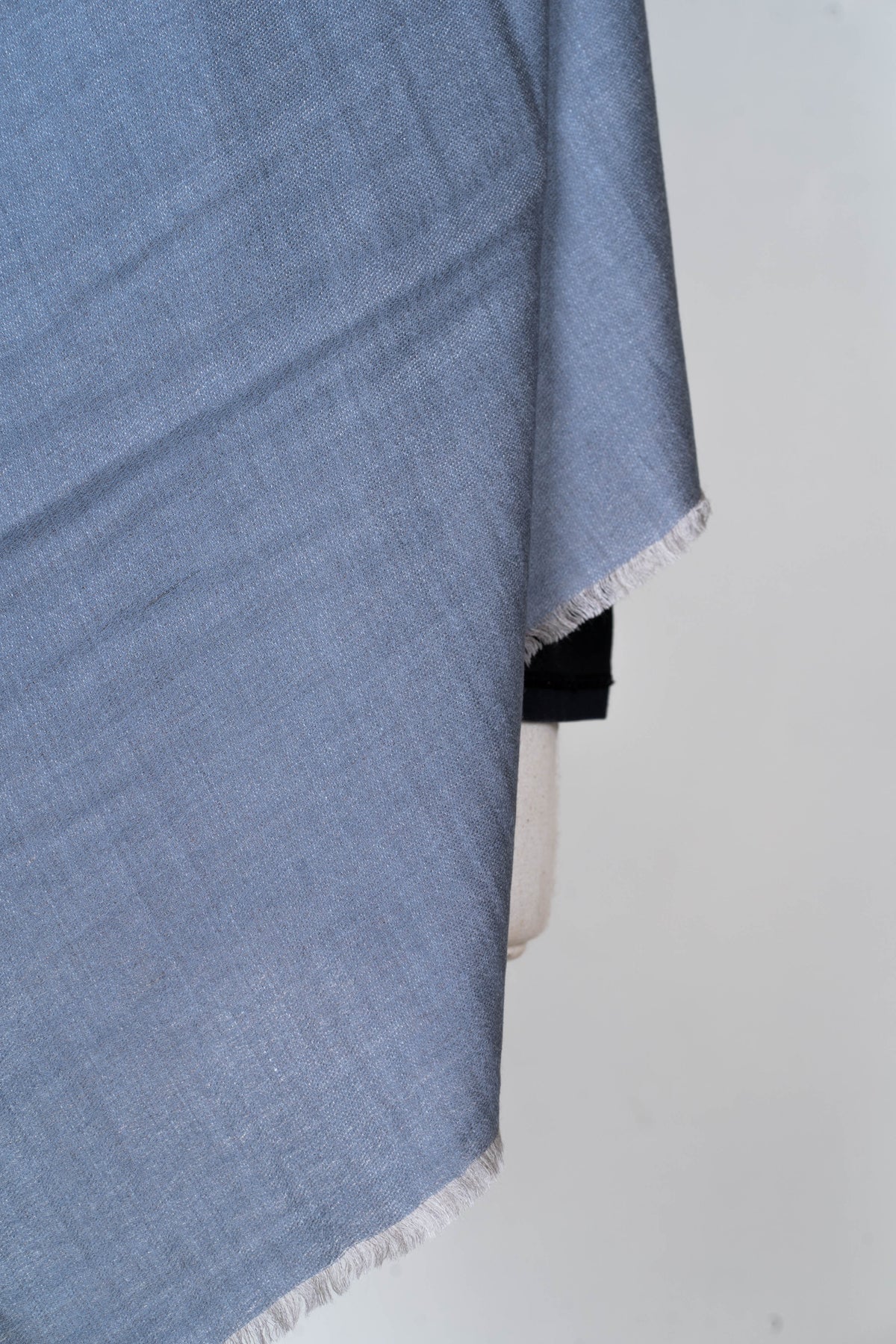 Close-up of the steel blue woven fabric and short pale fringe at the end of a Merino wool stole