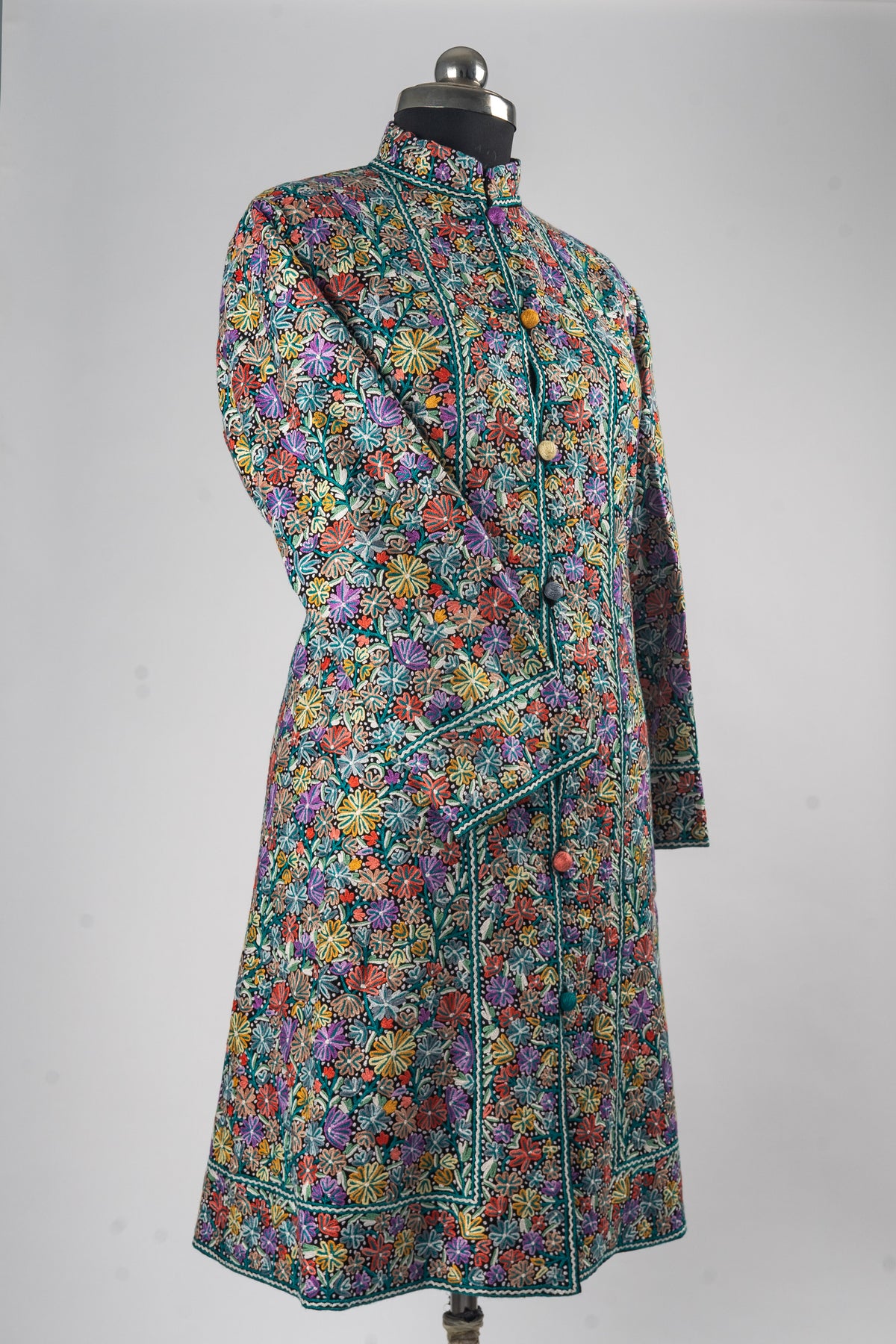 Angled full view of the long floral jacket on a mannequin with one sleeve crossed and turquoise-trimmed borders