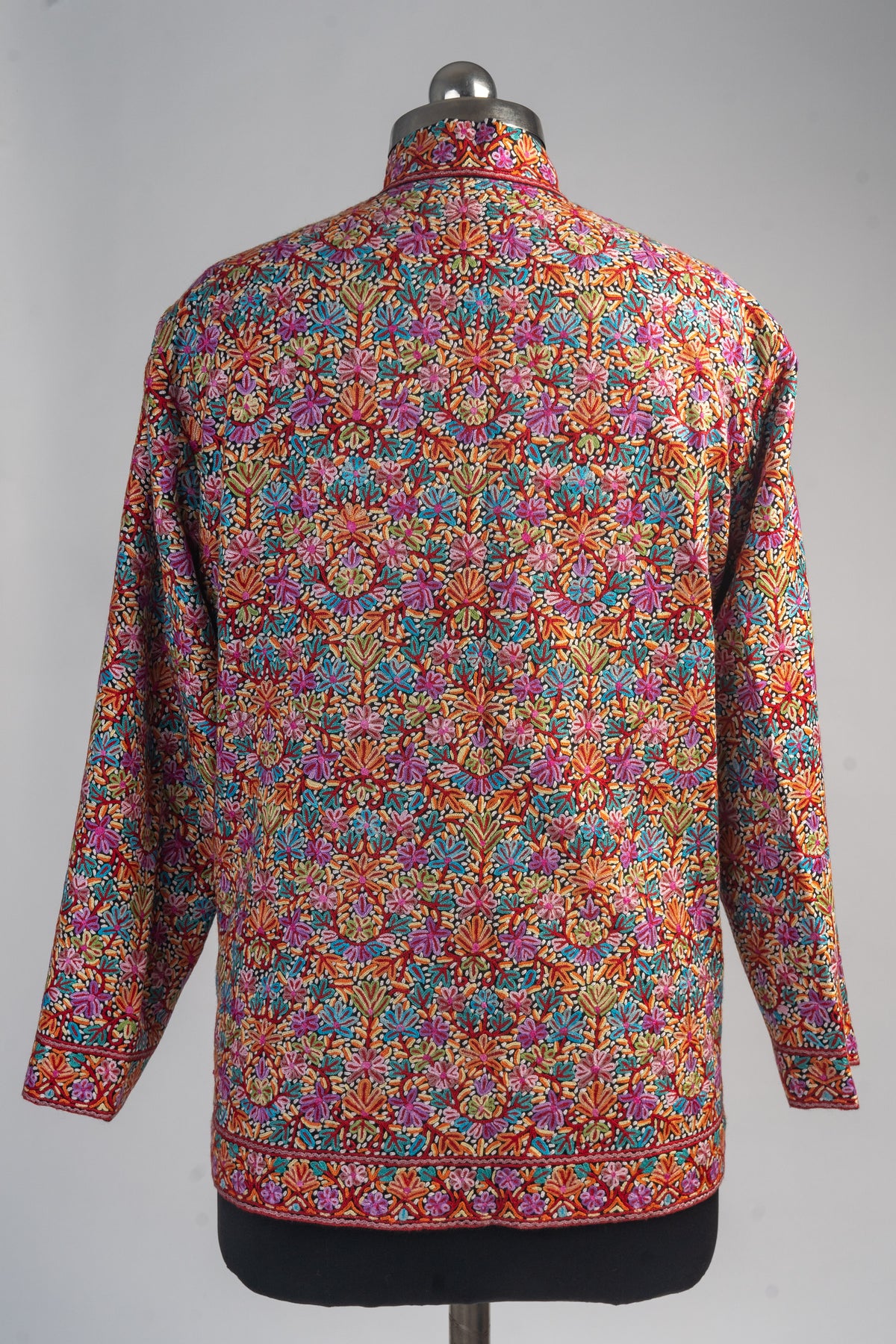 Back of the short merino wool jacket with dense multicoloured Aari floral embroidery and matching borders at the cuffs and hem.