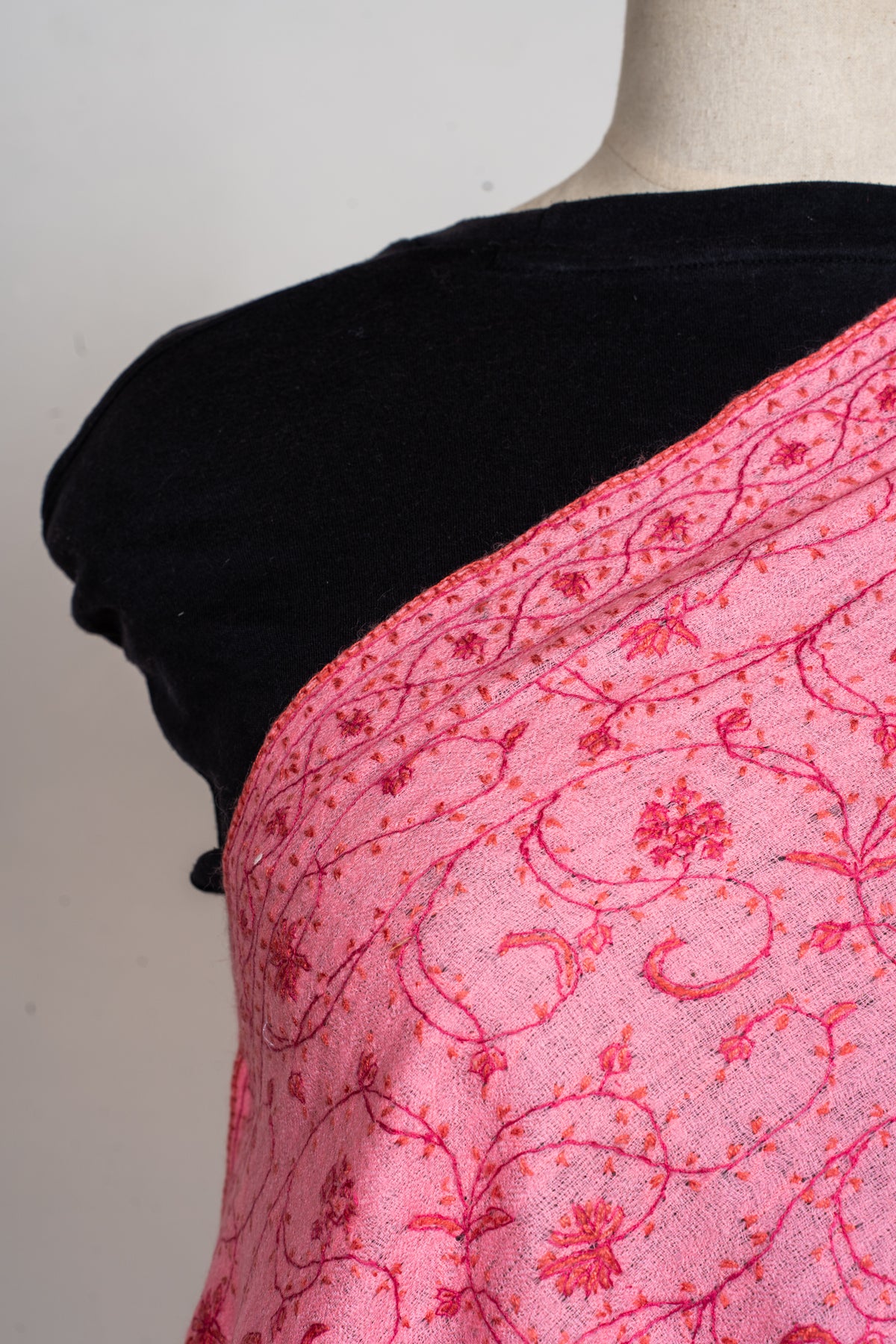 Close view of the pink stole’s floral vines and narrow patterned border along a mannequin’s shoulder
