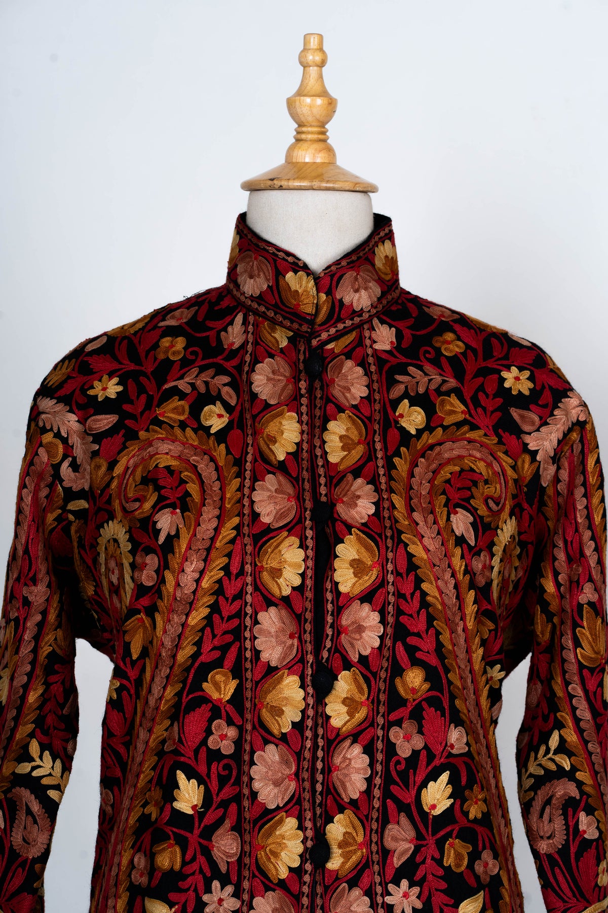 Close-up of the jacket upper front with a stand collar, paired floral bands and large red and gold paisley motifs.