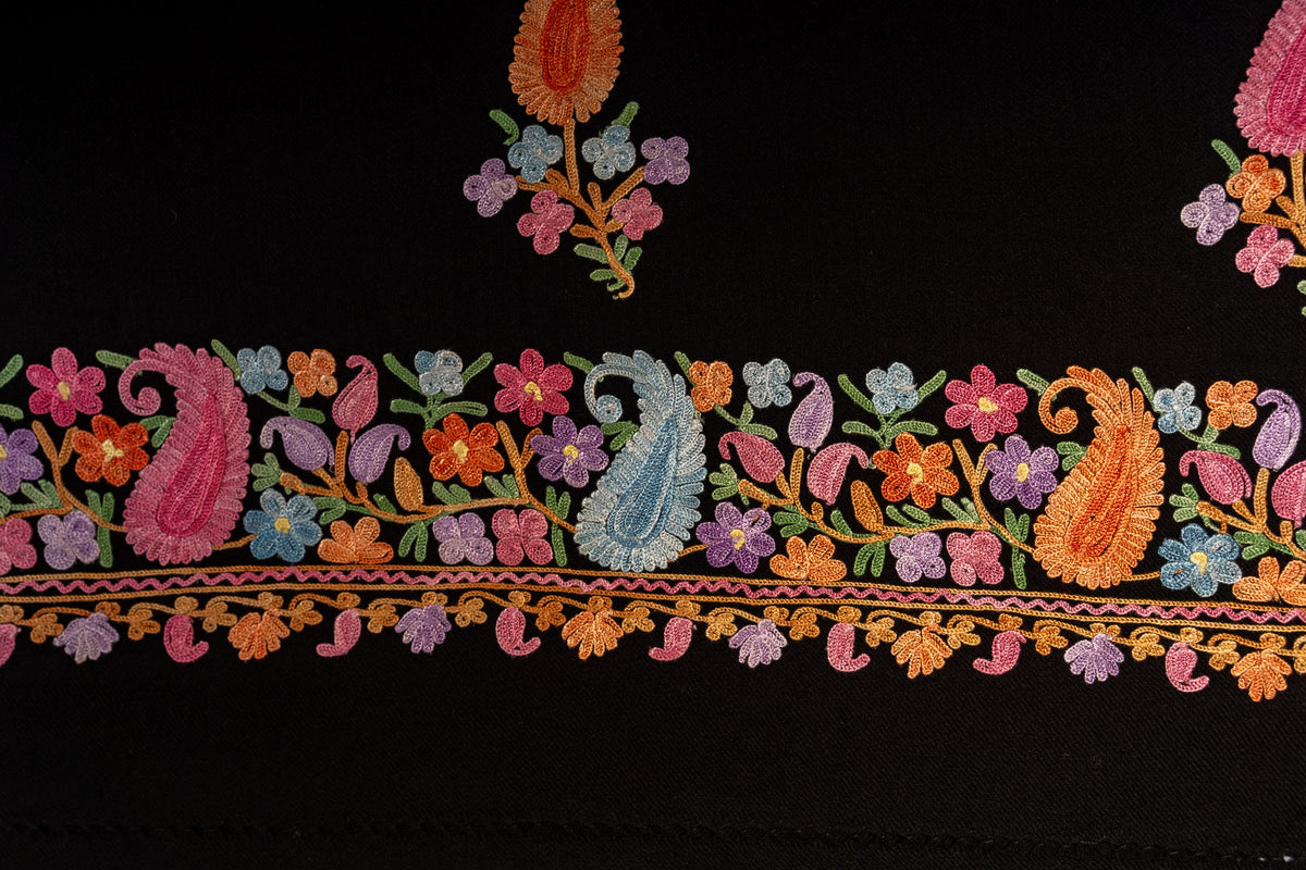 Flat detail of the black stole with pink, blue and orange paisleys among flowers along the end border.