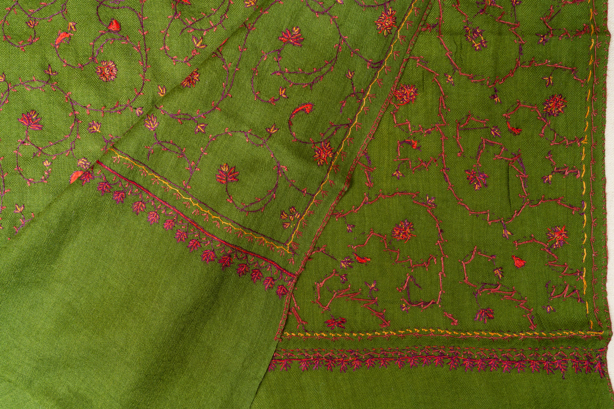 Folded olive-green stole corner showing overlapping floral vine embroidery, narrow gold-toned lines and pink pendant edging