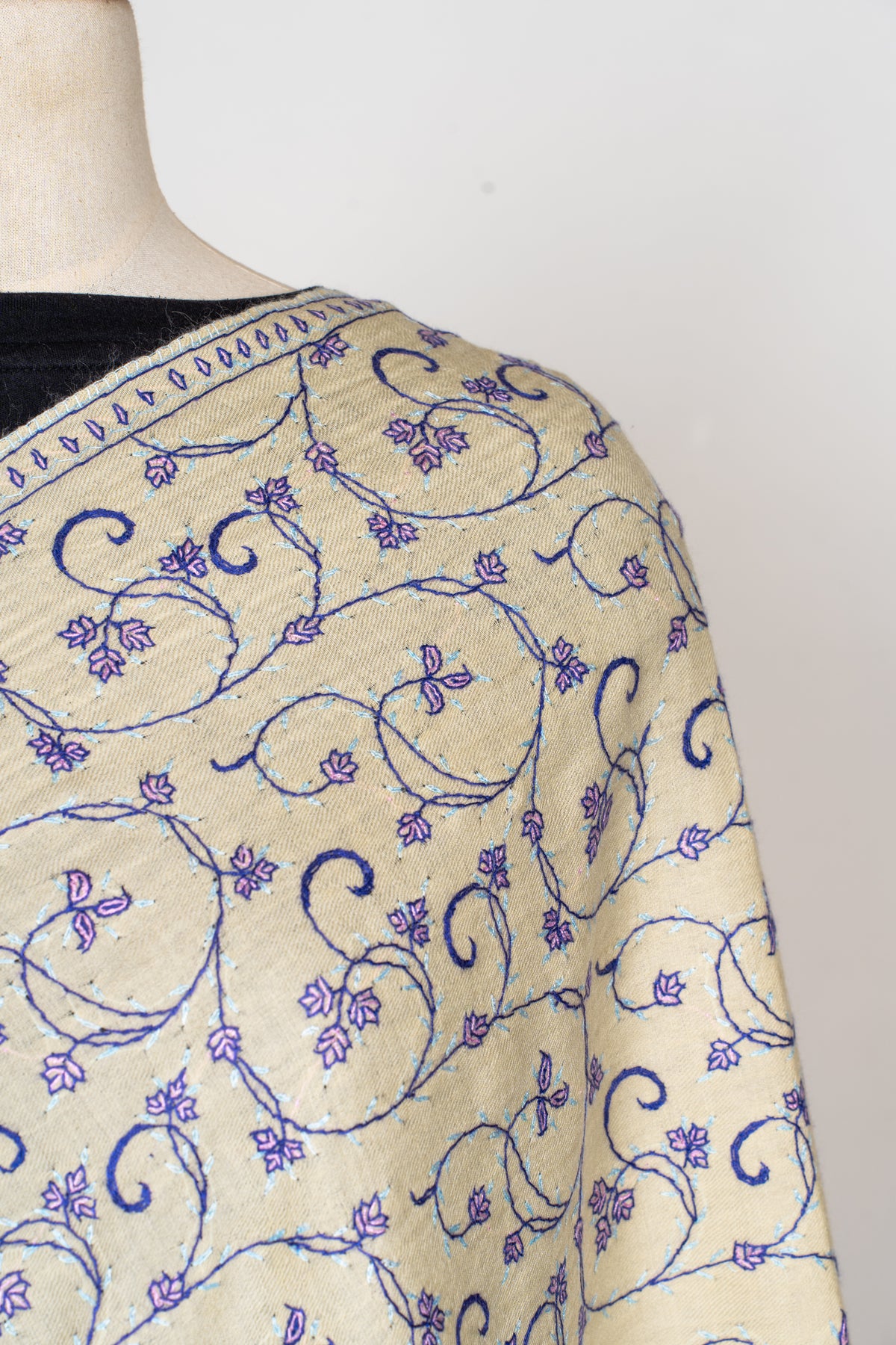 Shoulder detail of a cream stole embroidered with curling purple stems, small flowers and leaves