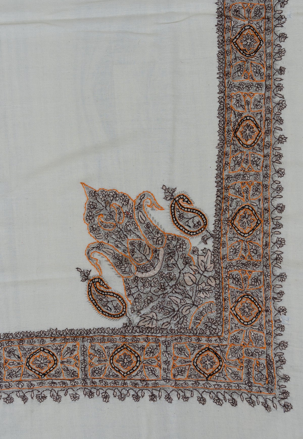 Corner of an ivory rumal with charcoal and ochre Sozni paisley and floral embroidery beside a geometric border