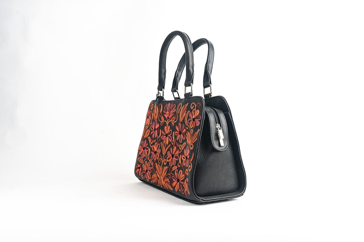 Three-quarter side view of a black handbag with an orange-pink embroidered front, two handles and a plain gusset