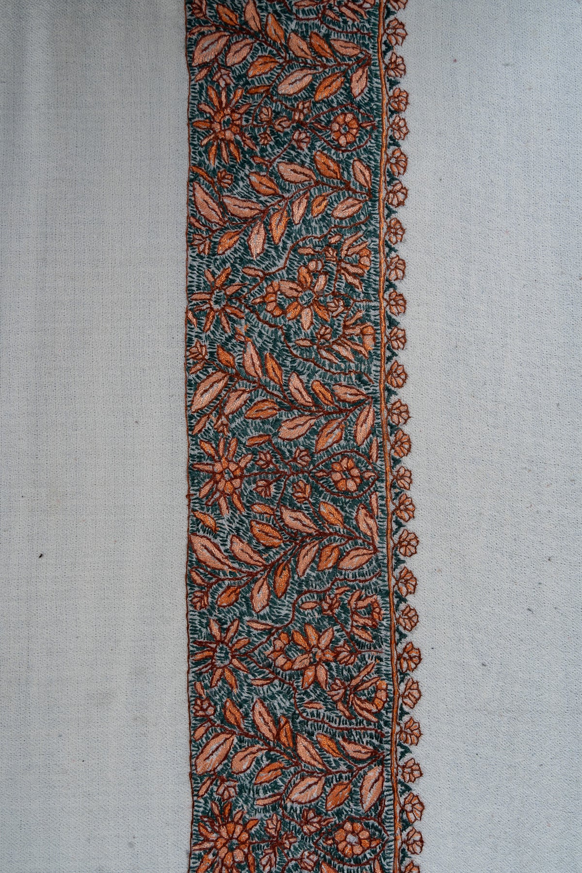 Dense teal and orange Sozni flowers and leafy vines along the broad border of an ivory rumal